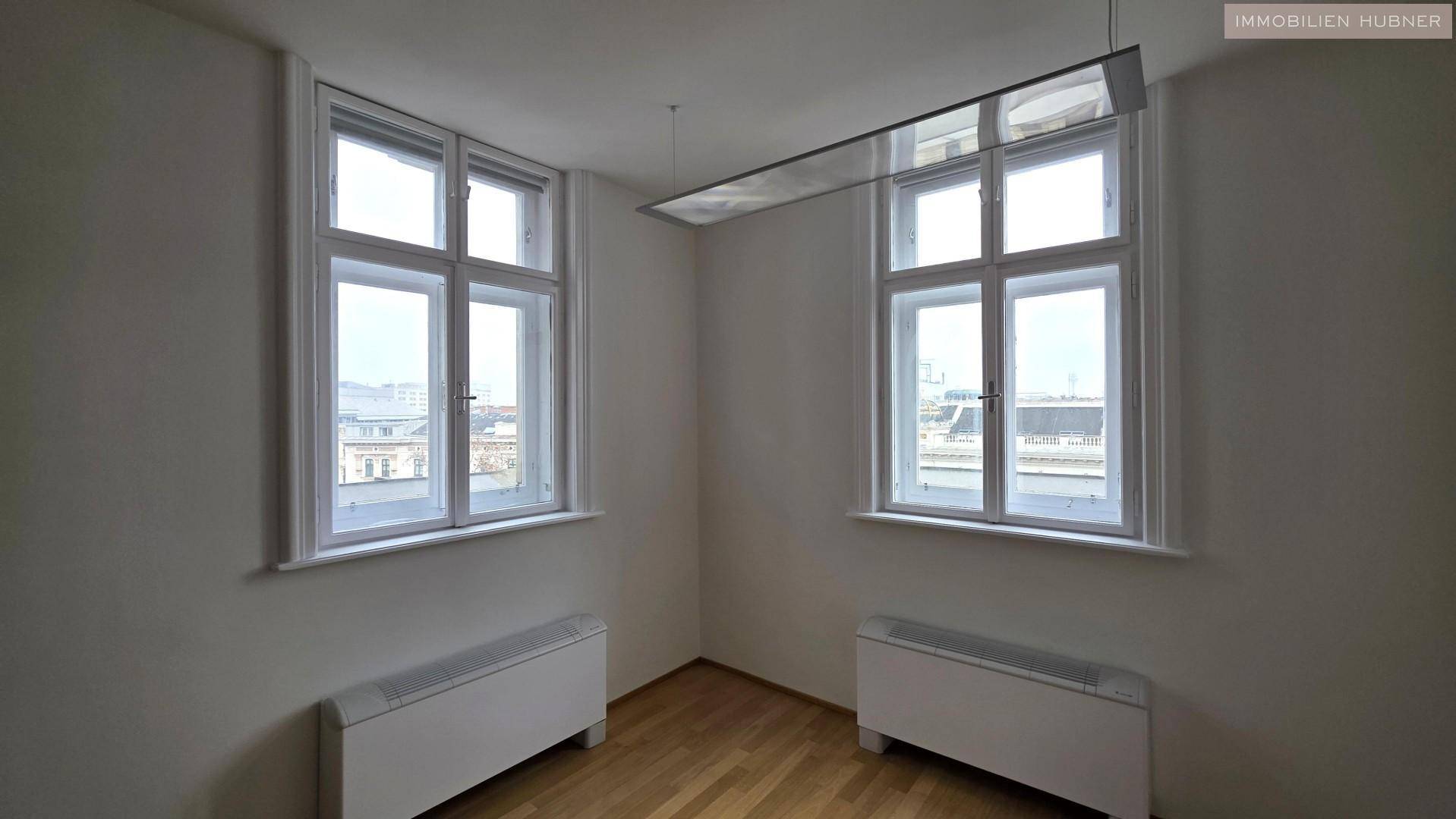 Eckbereich eines Büros mit zwei großen Fenstern, die viel Licht hereinlassen, und Heizkörpern darunter.
