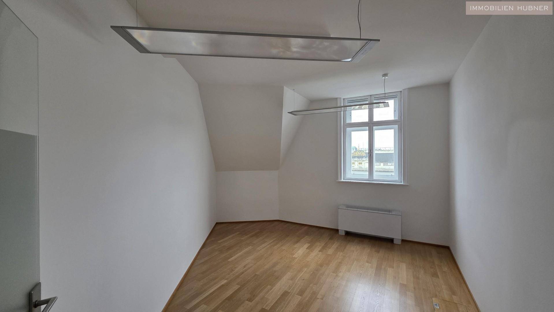 Heller Büroraum mit schrägen Wänden, Holzparkettboden und einem Fenster, das die Stadt überblickt.