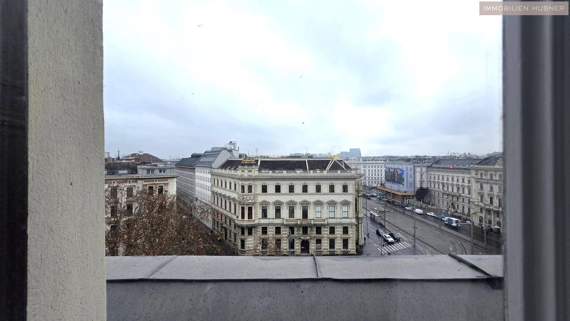 Blick aus dem Fenster auf eine belebte Stadtstraße mit historischen Gebäuden und Verkehr.