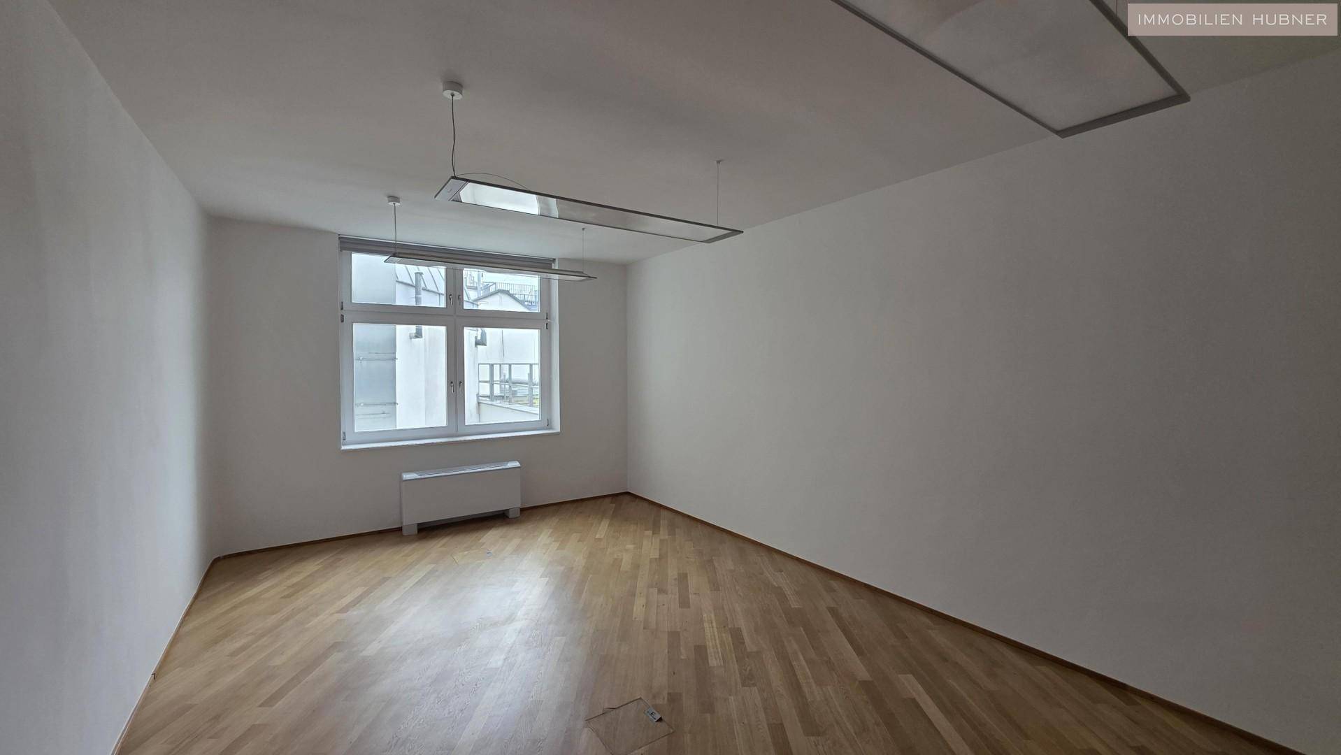 Geräumiges, leeres Büro mit Holzparkettboden und einem großen Fenster, das für natürliche Beleuchtung sorgt.