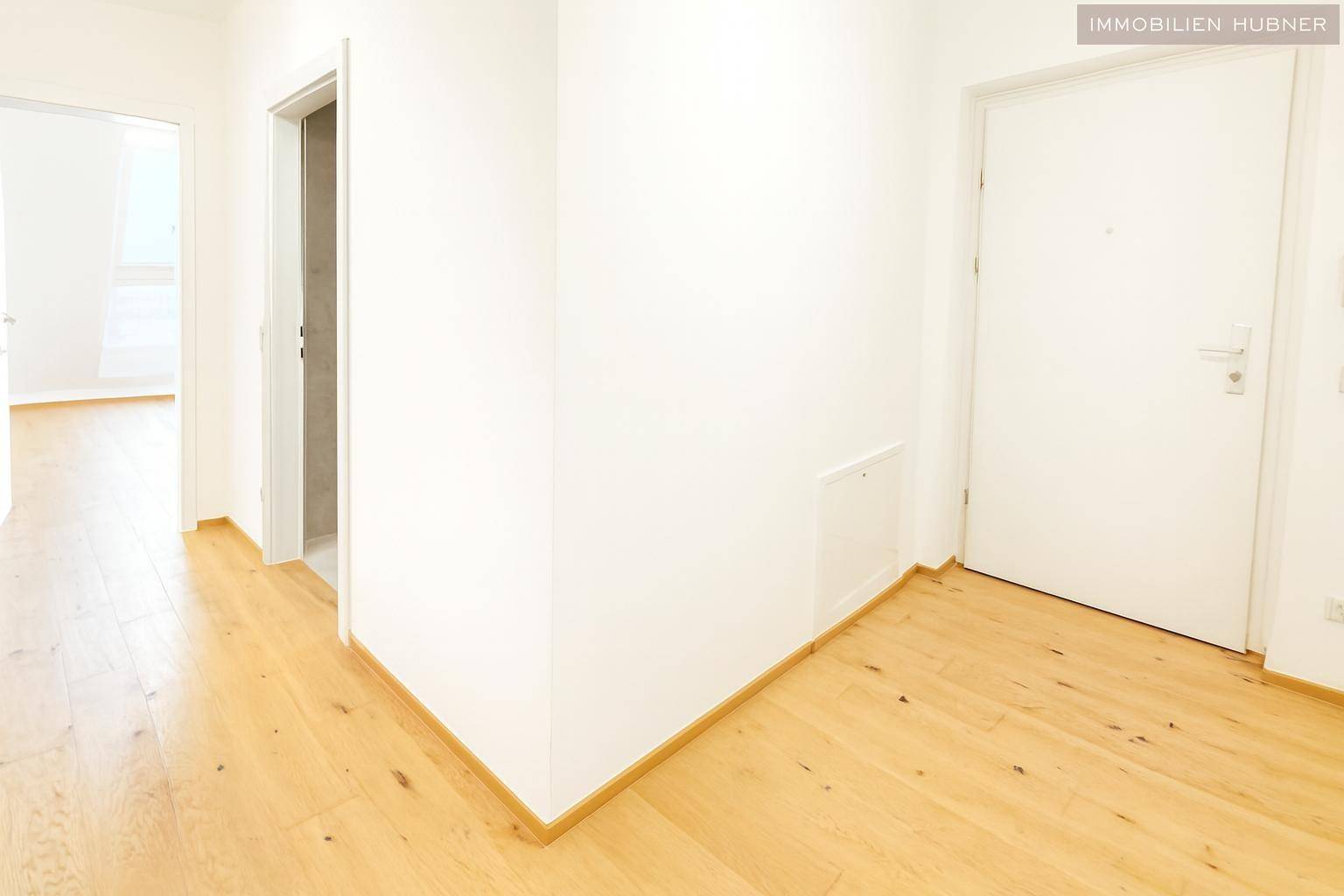 Heller Flur mit Holzboden und weißen Wänden, der zu weiteren Räumen führt.
