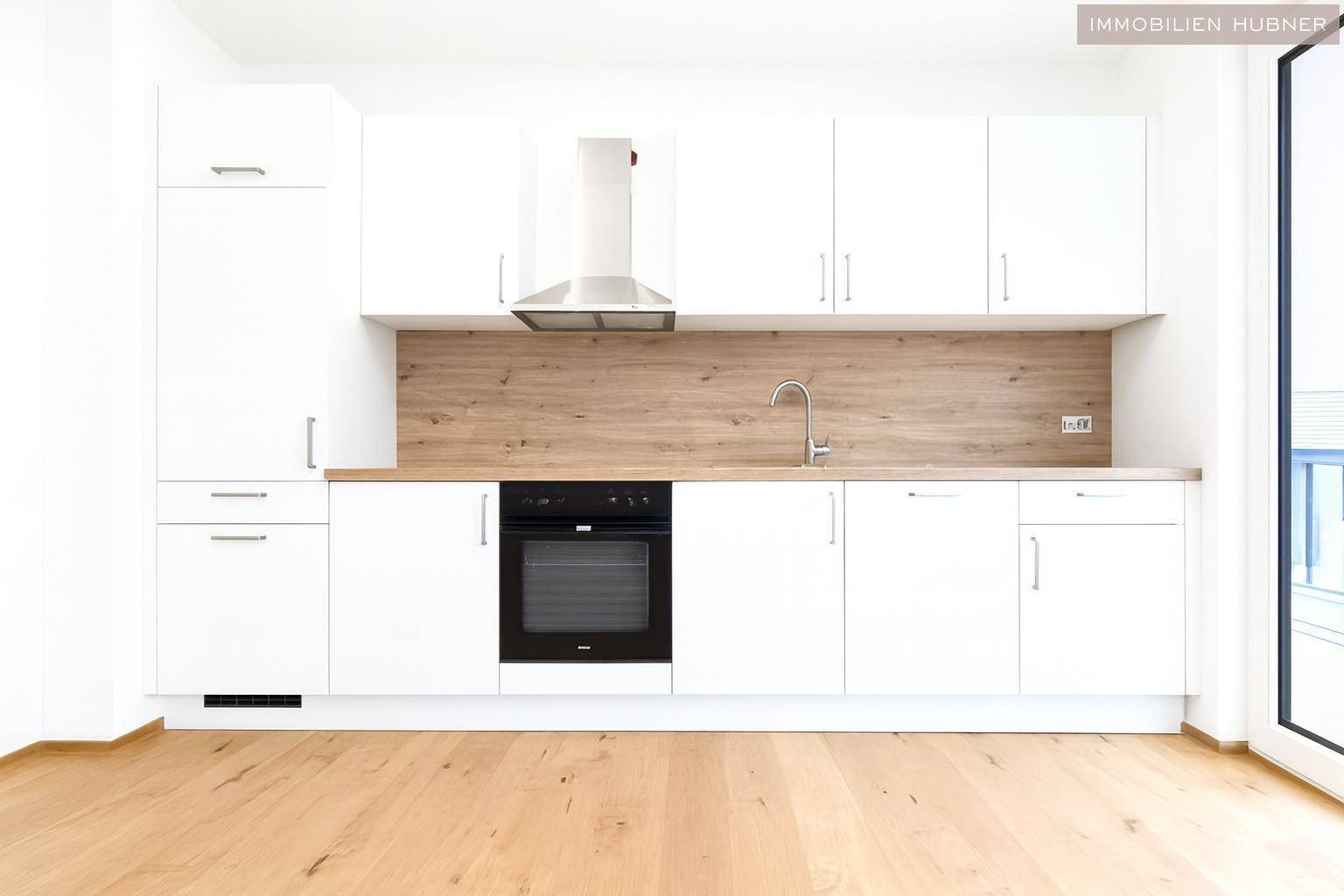 Neue Einbauküche mit weißen Schränken, Holz-Arbeitsplatte und integriertem Backofen und Dunstabzugshaube.