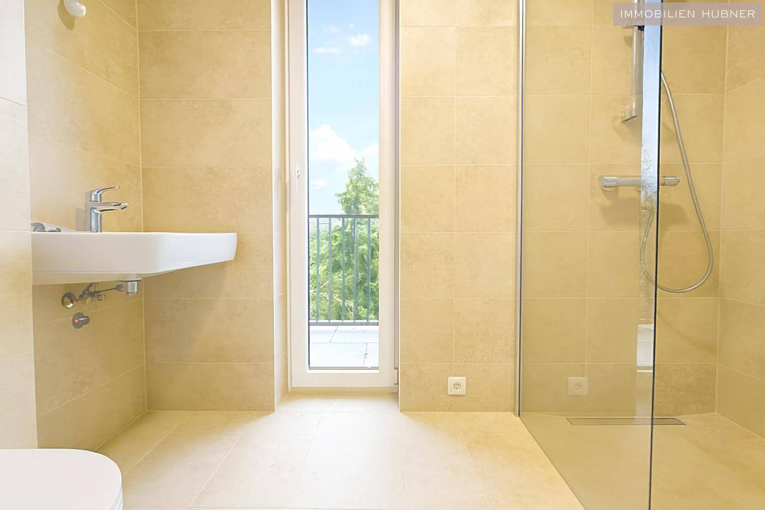 Modernes Badezimmer mit beigefarbenen Fliesen, Waschbecken und ebenerdiger Dusche mit Glasabtrennung.