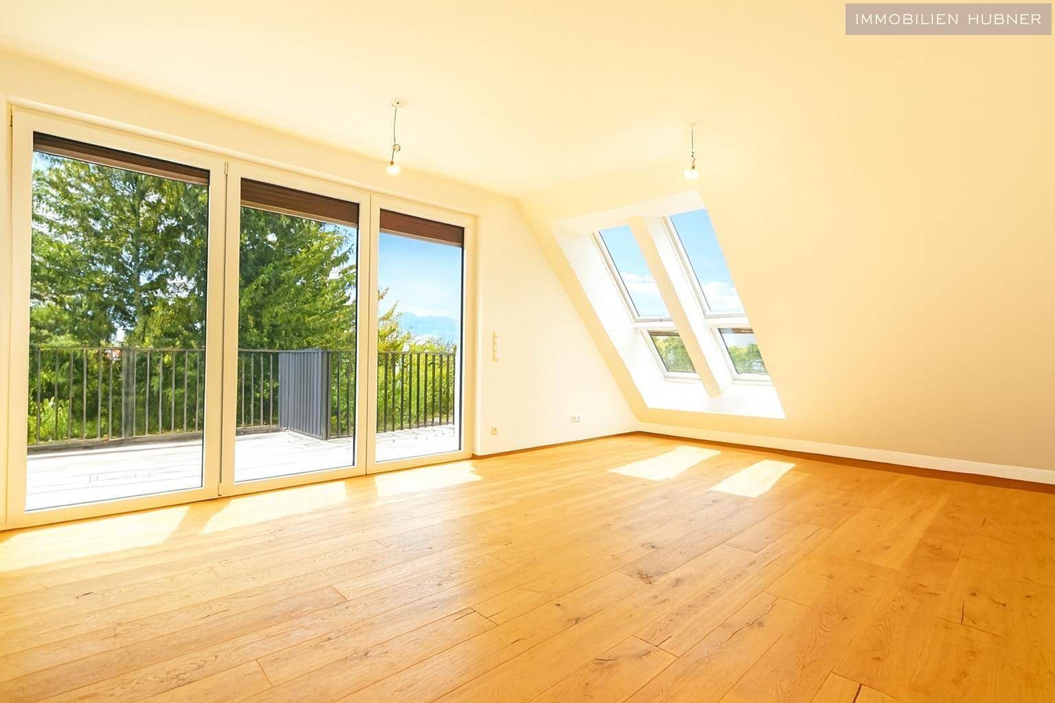 Lichtdurchfluteter Wohnbereich mit Holzboden, großen Fenstern und zusätzlichen Dachfenstern für viel Helligkeit.