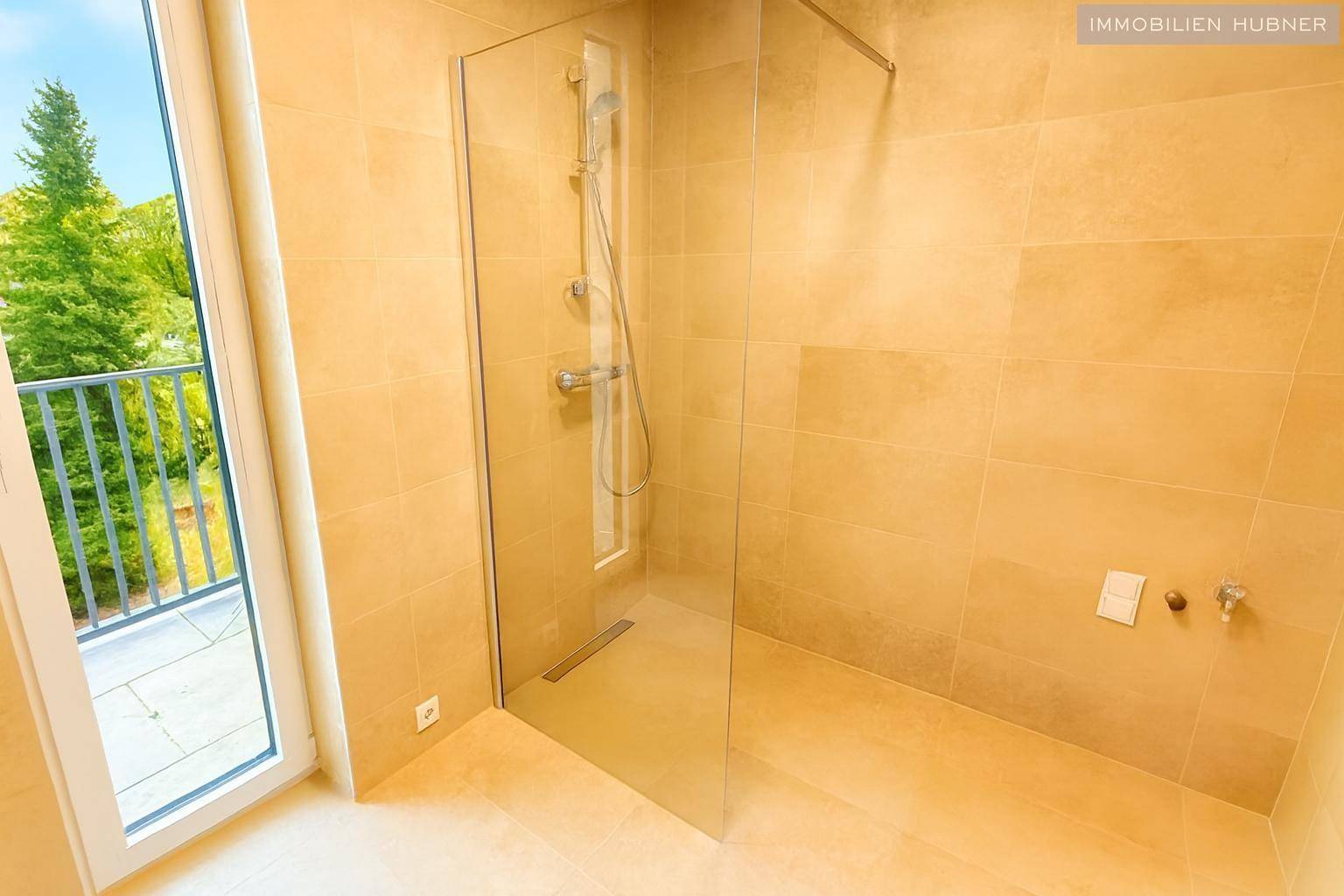 Helles Badezimmer mit beigefarbenen Fliesen, ebenerdiger Dusche und Zugang zu einem kleinen Balkon.
