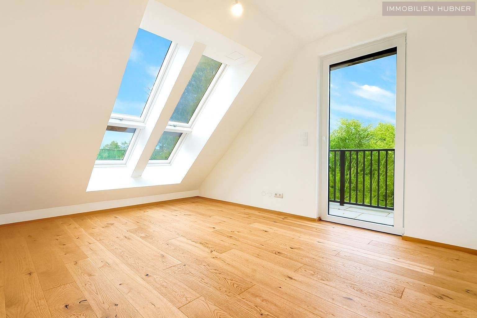 Helles Zimmer mit Holzboden, Dachschrägen, Dachfenstern und Zugang zu einem kleinen französischen Balkon.