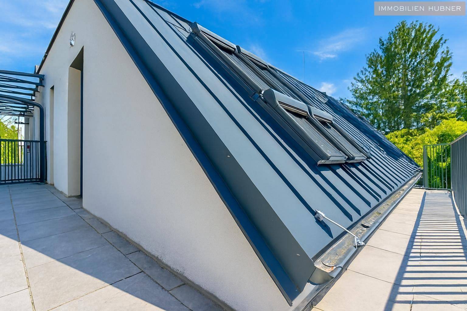 Modernes Gebäude mit schrägem Dach, Dachfenstern und einer großen gefliesten Terrasse.