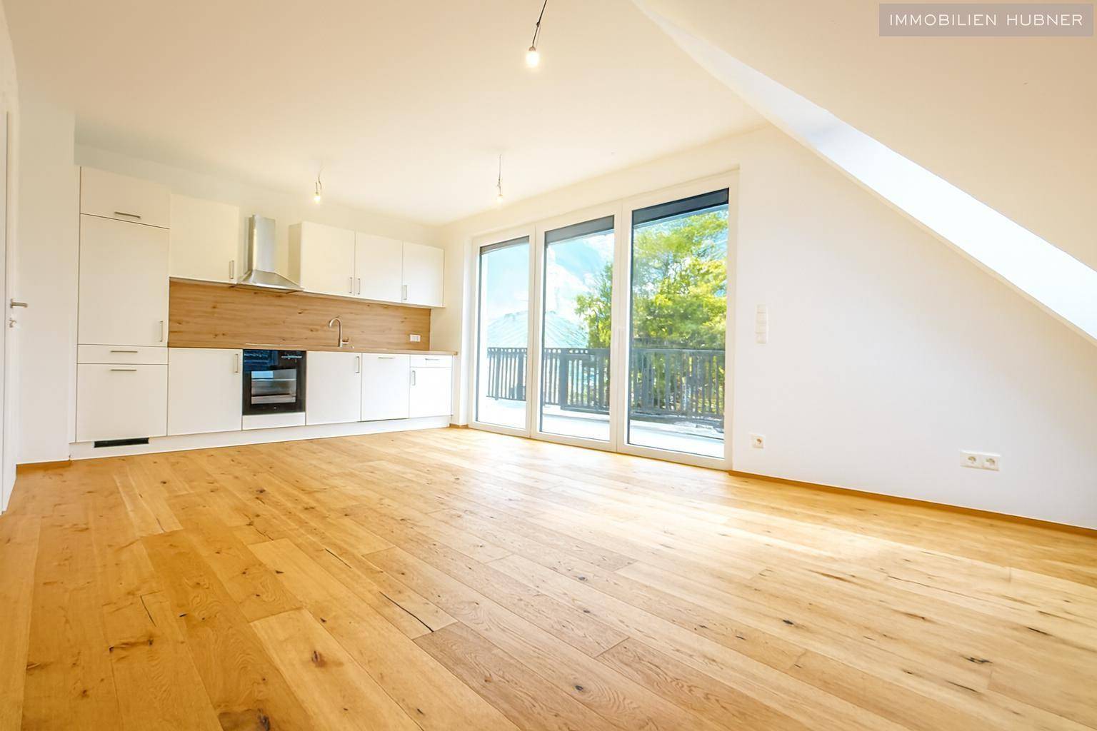 Heller offener Wohnbereich mit integrierter Küche, Holzboden und Zugang zu einer großen Terrasse.