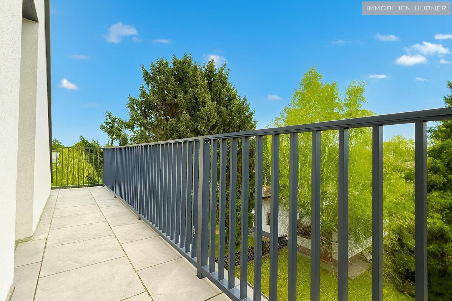 Lange geflieste Terrasse mit Metallgeländer und Blick auf grüne Bäume und die Umgebung.