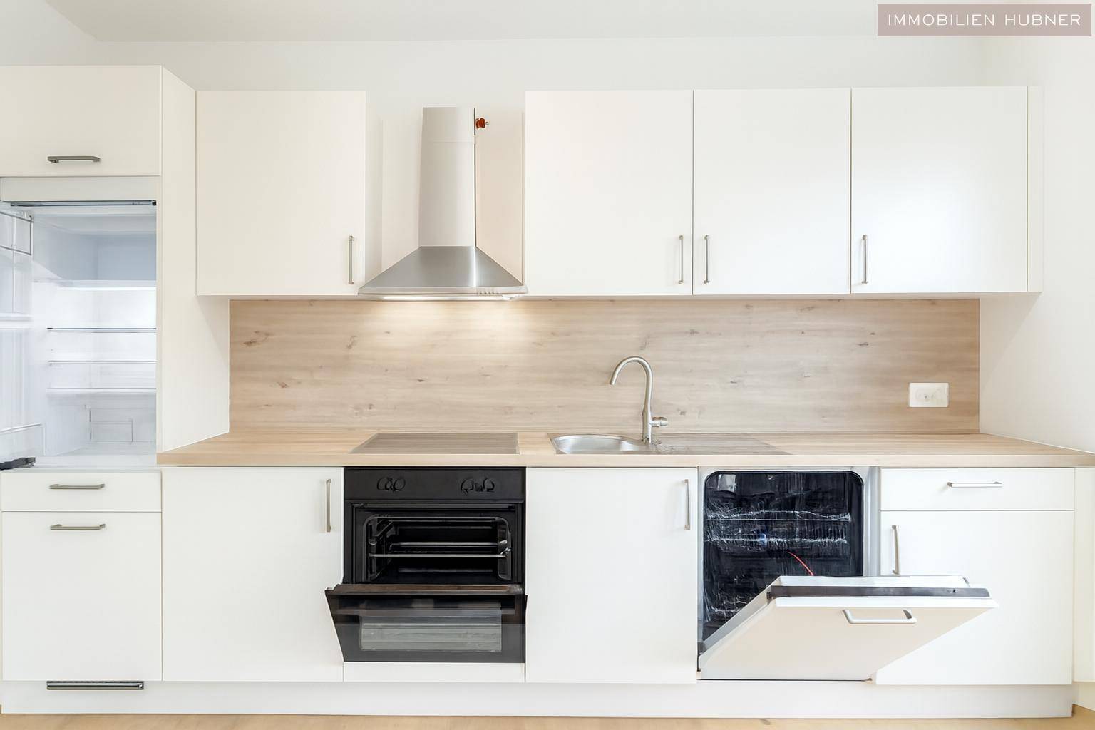 Voll ausgestattete moderne Küche mit weißen Fronten, Holz-Arbeitsplatte, Backofen, Kühlschrank und Geschirrspüler.