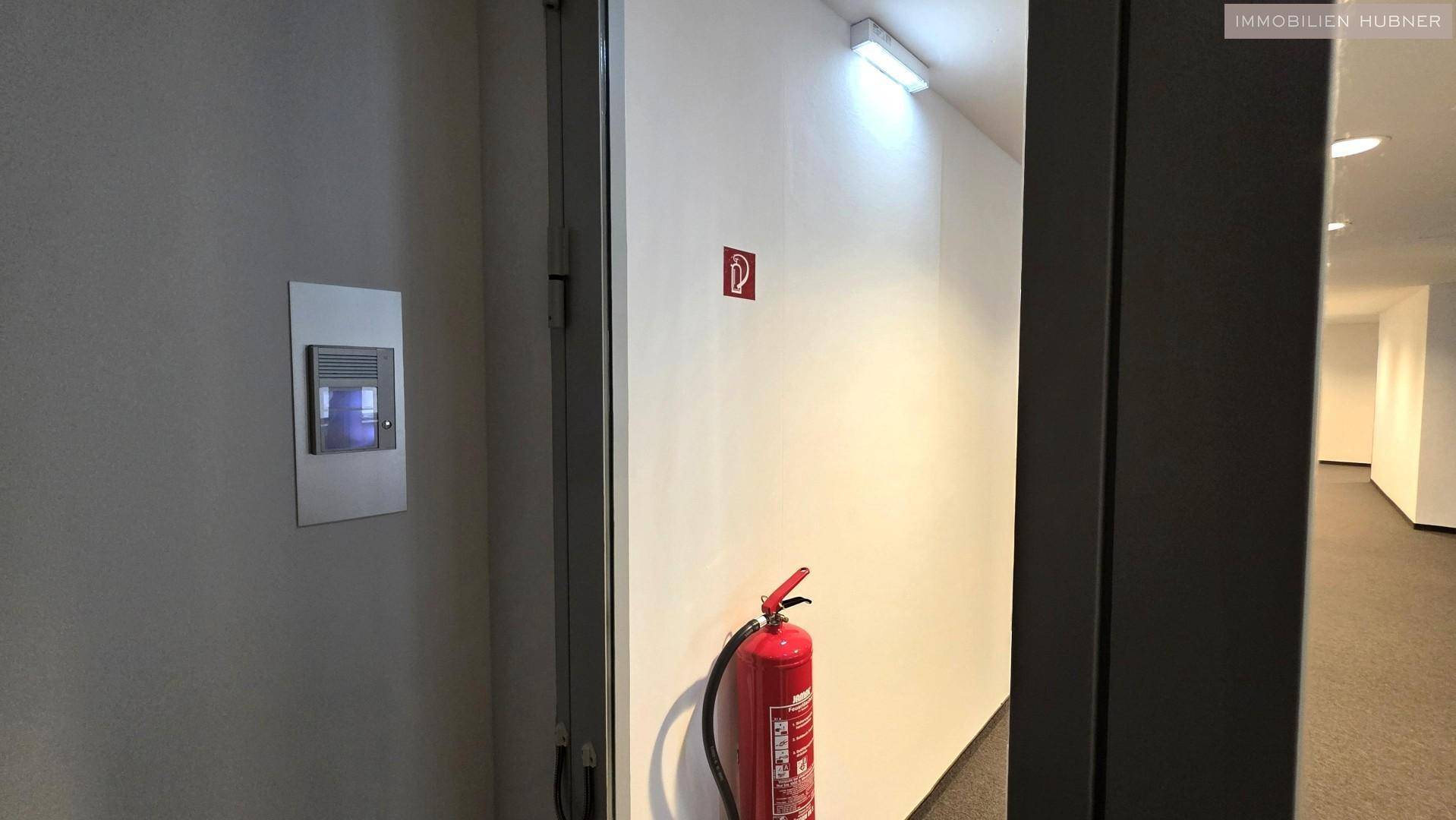 Heller Flur mit Gegensprechanlage und einem roten Feuerlöscher an der Wand.