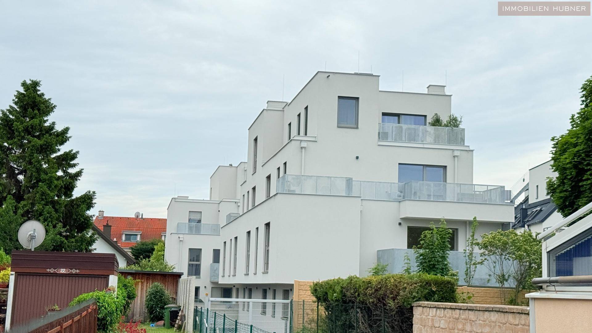 Moderne Wohnanlage mit weißer Fassade, großen Fenstern und mehreren Balkonen unter bewölktem Himmel.