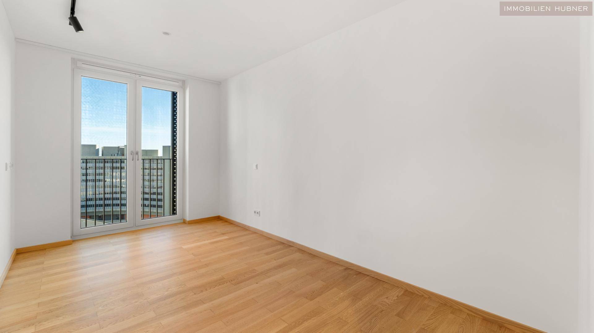 Helles Schlafzimmer mit Parkettboden und Zugang zu einem französischen Balkon.