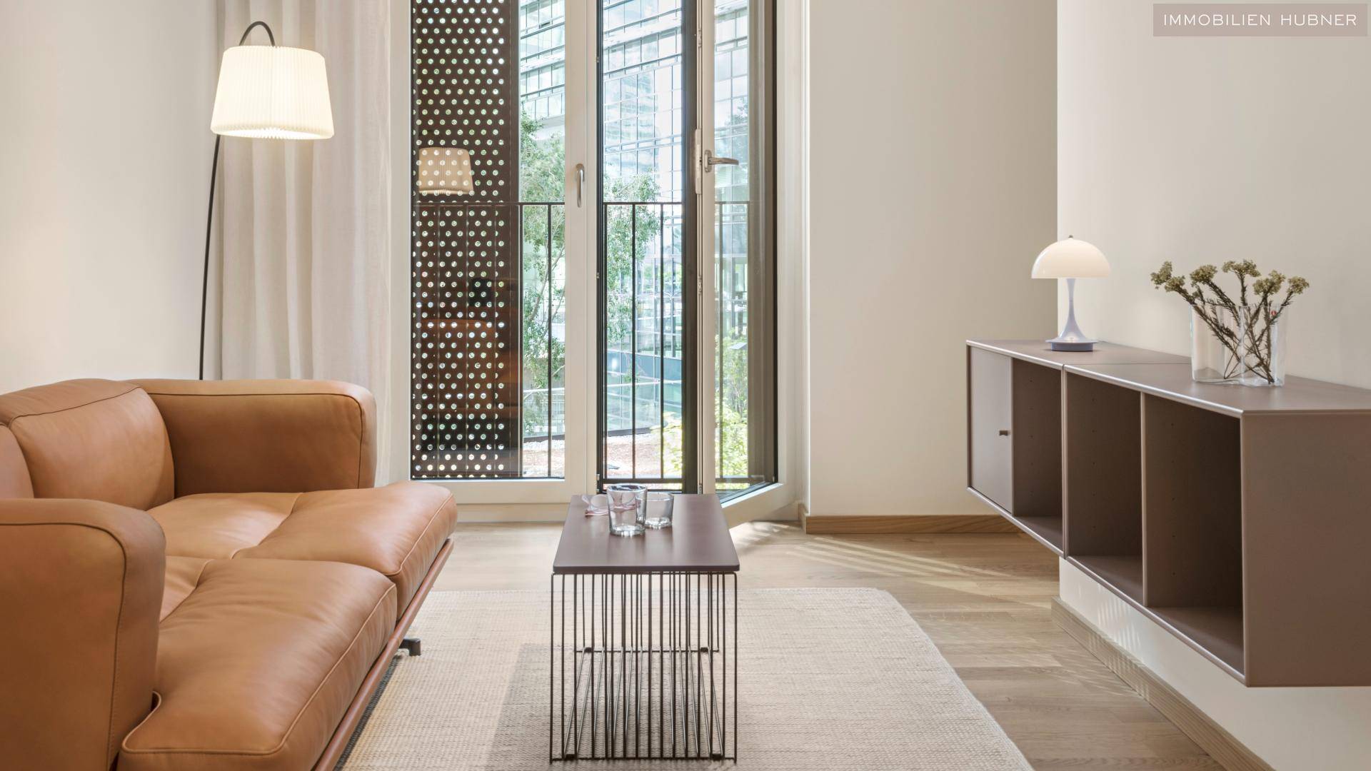 Gemütlicher Wohnbereich mit Ledersofa, modernem Beistelltisch und Zugang zum Balkon.