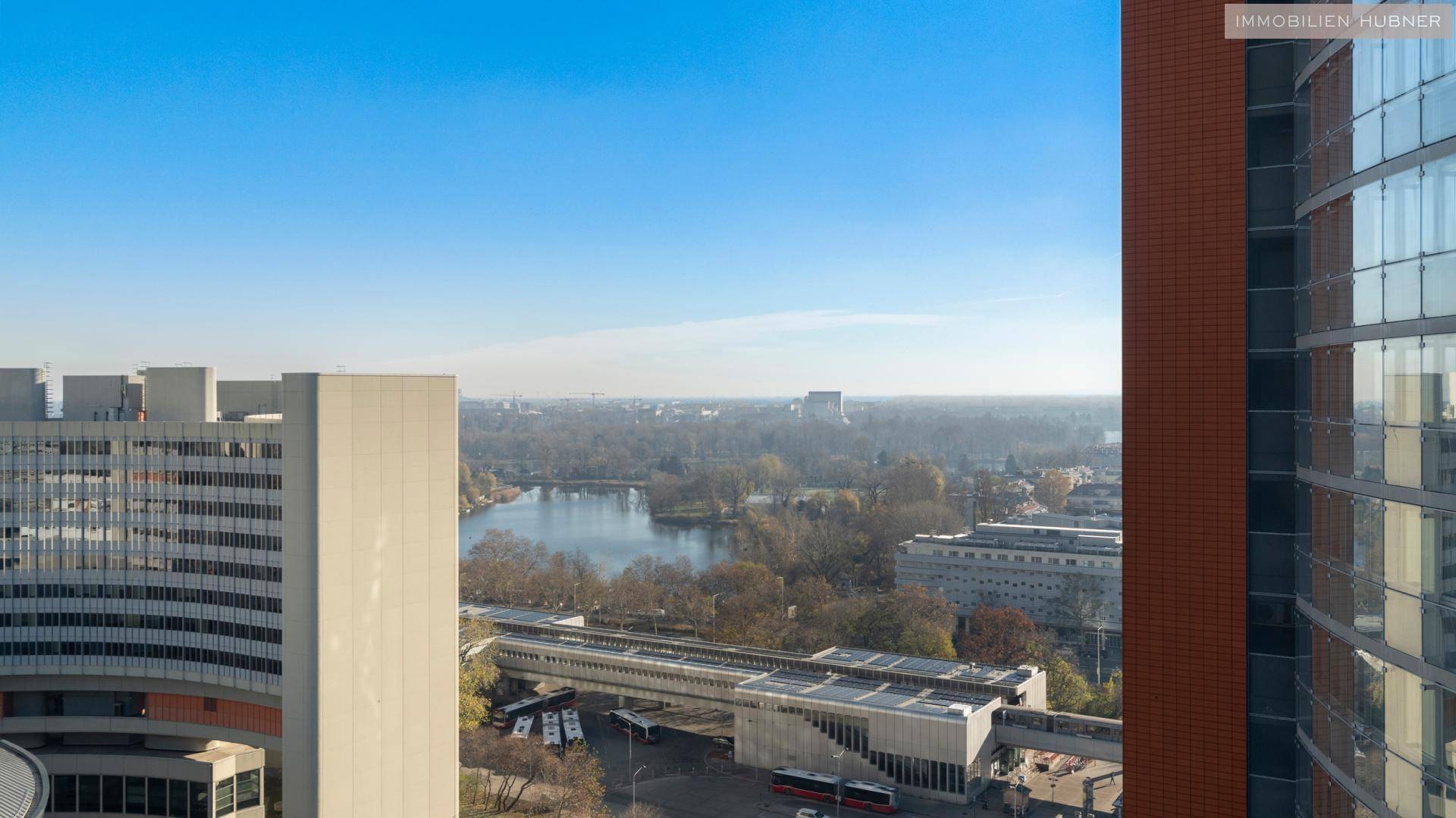 Weitläufiger Blick über die Stadt mit einem See und umliegenden Grünflächen.