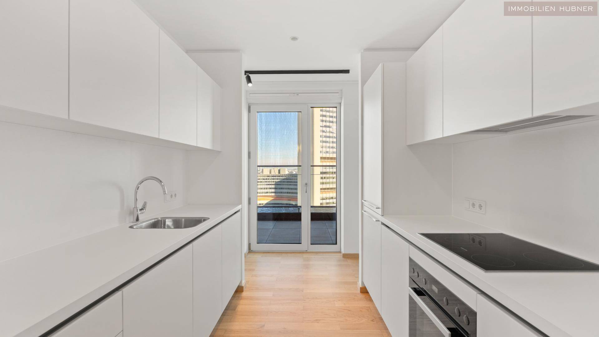 Moderne weiße Küche mit Einbaugeräten, Parkettboden und Zugang zum Balkon.