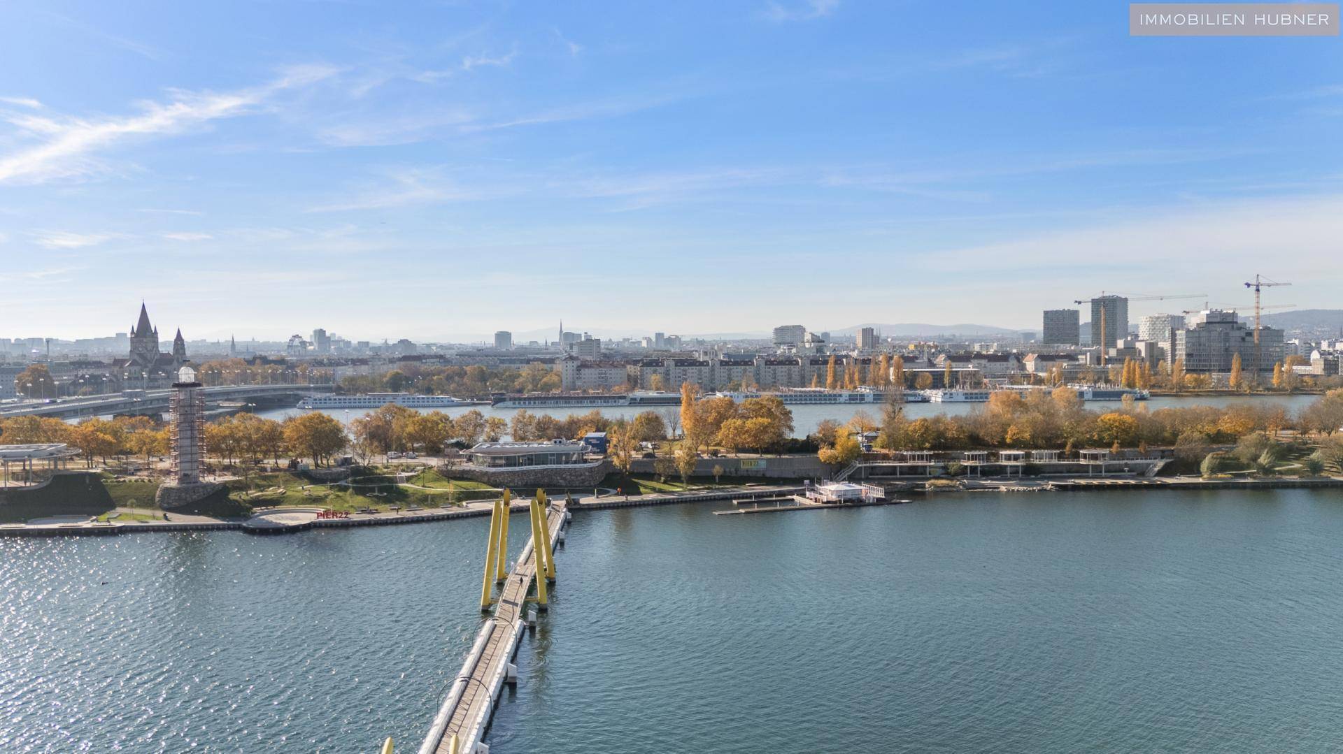 Weitläufiger Blick über die Donau und die Wiener Skyline an einem sonnigen Tag.