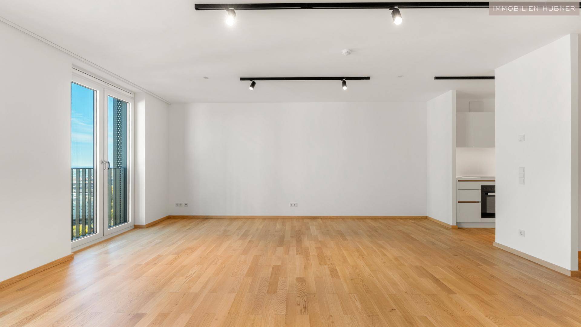 Heller Wohnbereich mit Parkettboden, modernen Deckenleuchten und Zugang zu einem französischen Balkon.