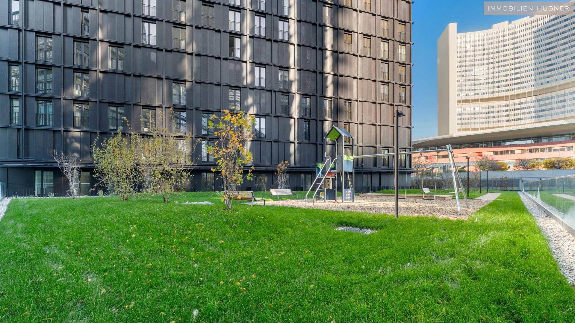 Grüner Gemeinschaftsgarten mit Spielplatz vor einem modernen Wohngebäude.
