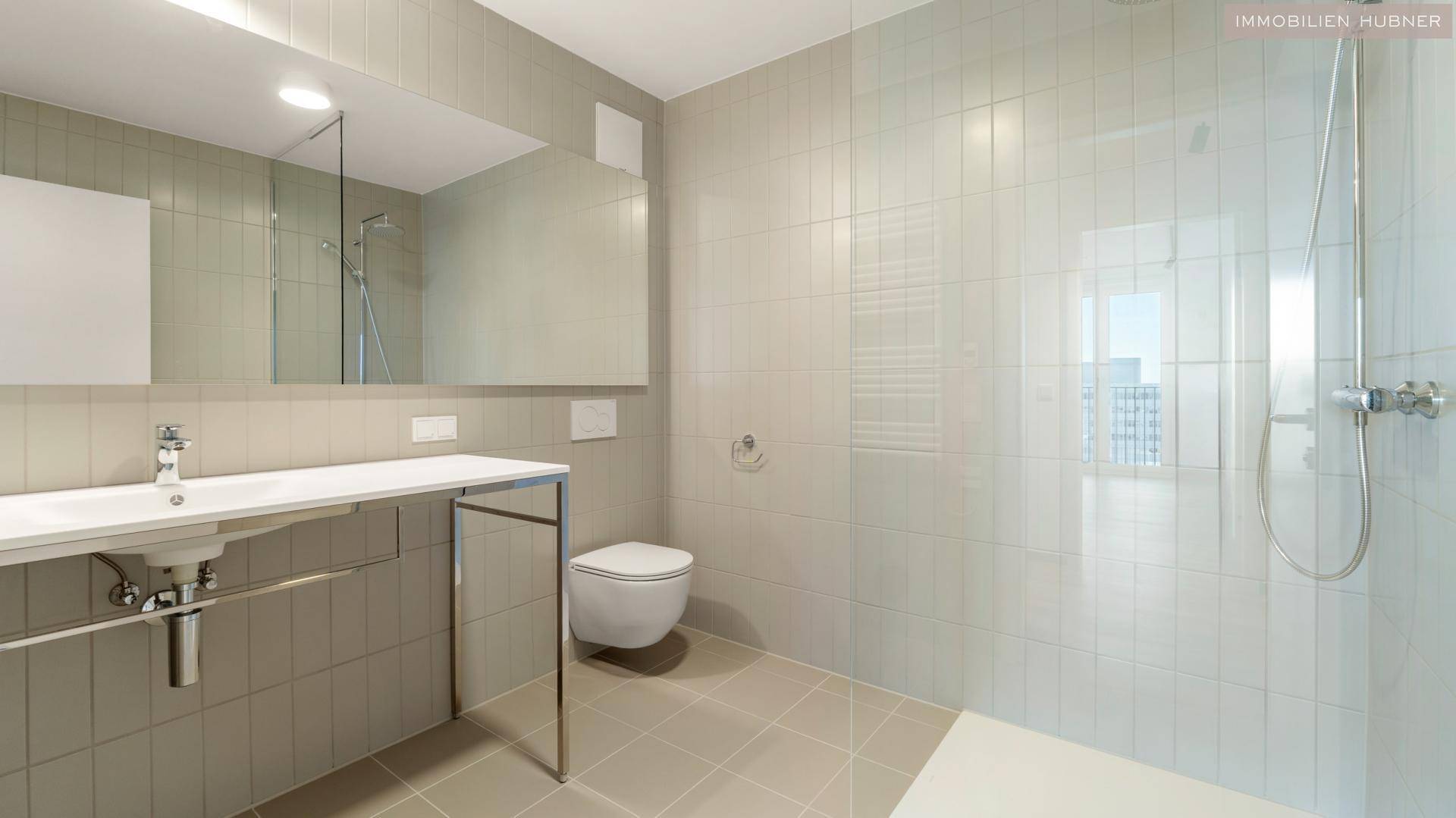 Helles Badezimmer mit Dusche, WC und großem Spiegel über dem Waschtisch.