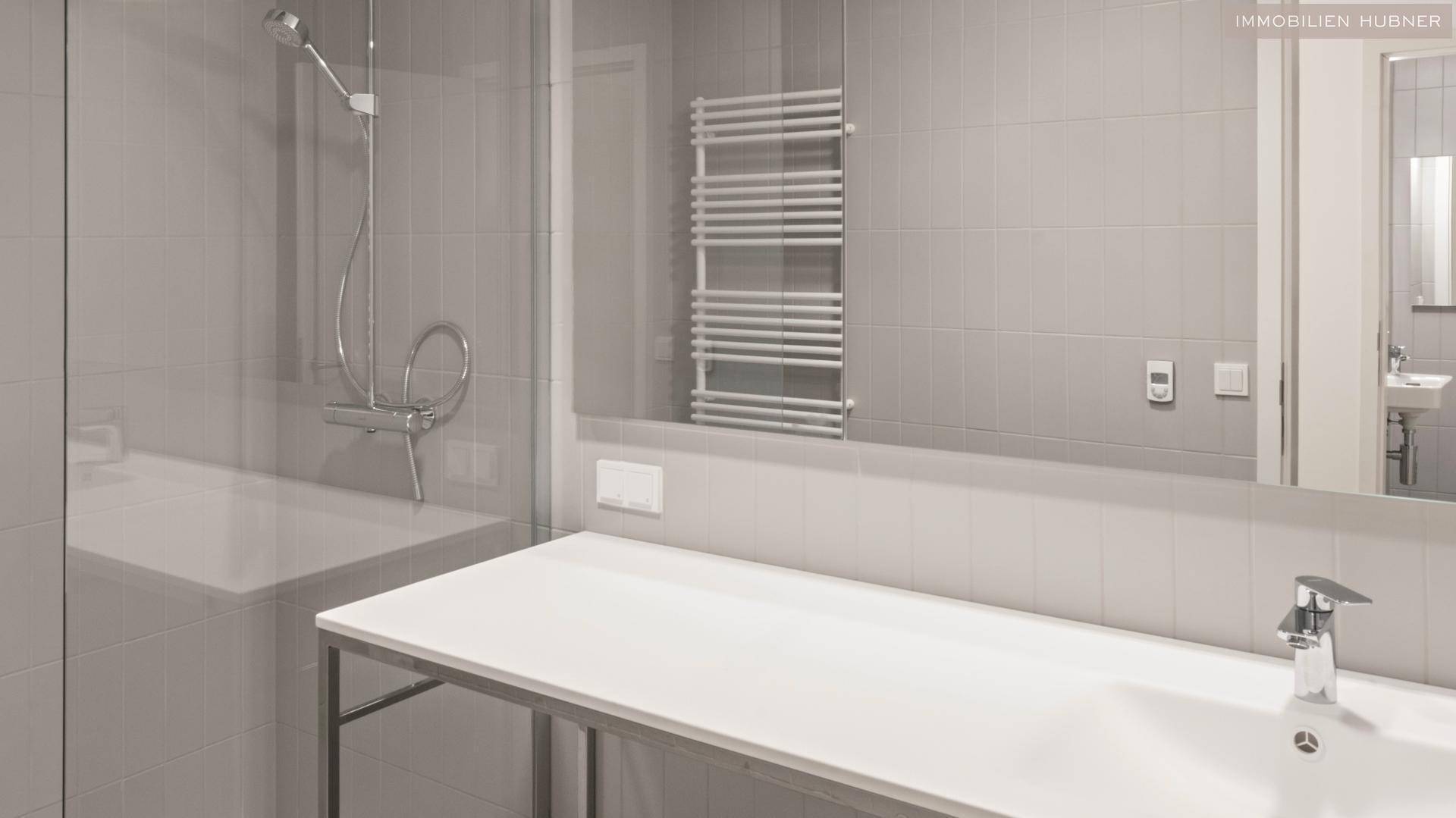 Modernes Badezimmer mit grauen Fliesen, großer Dusche und beheiztem Handtuchhalter.
