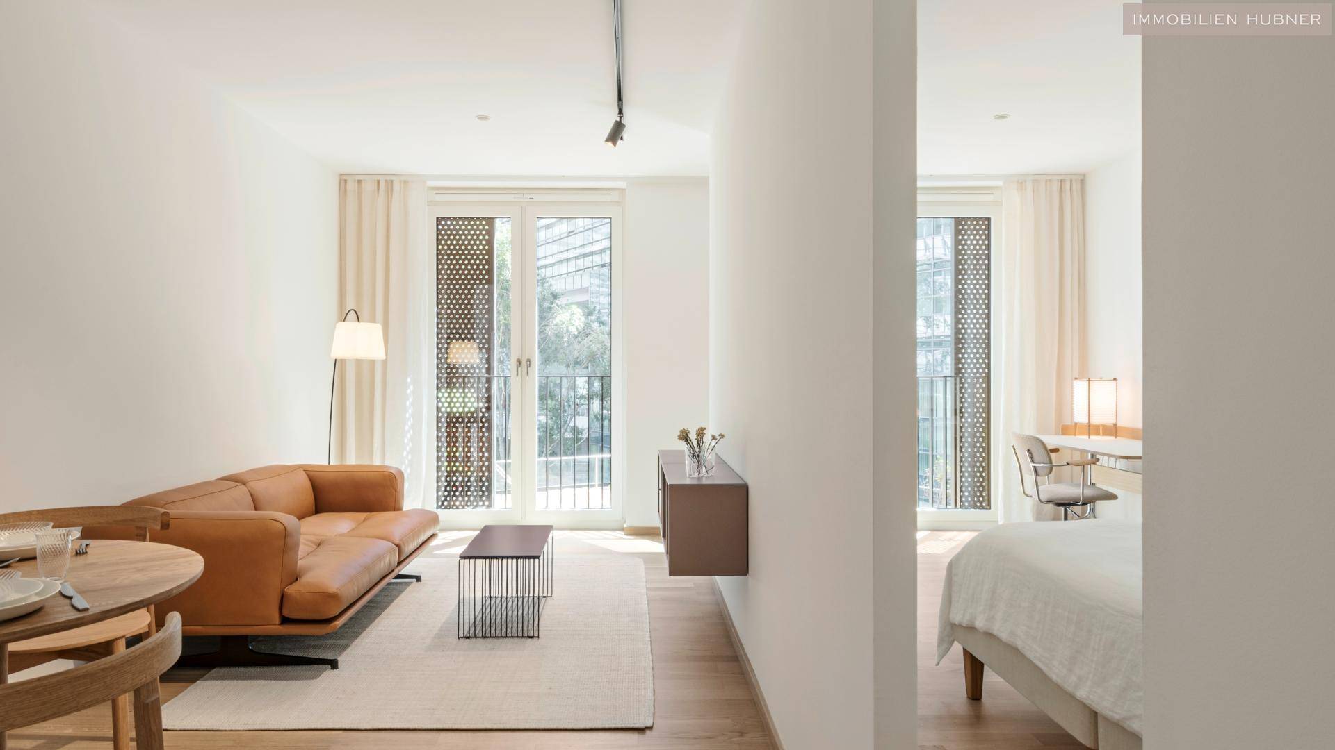 Gemütlicher Wohnbereich mit Ledersofa und Zugang zu einem französischen Balkon, daneben ein Schlafzimmer.