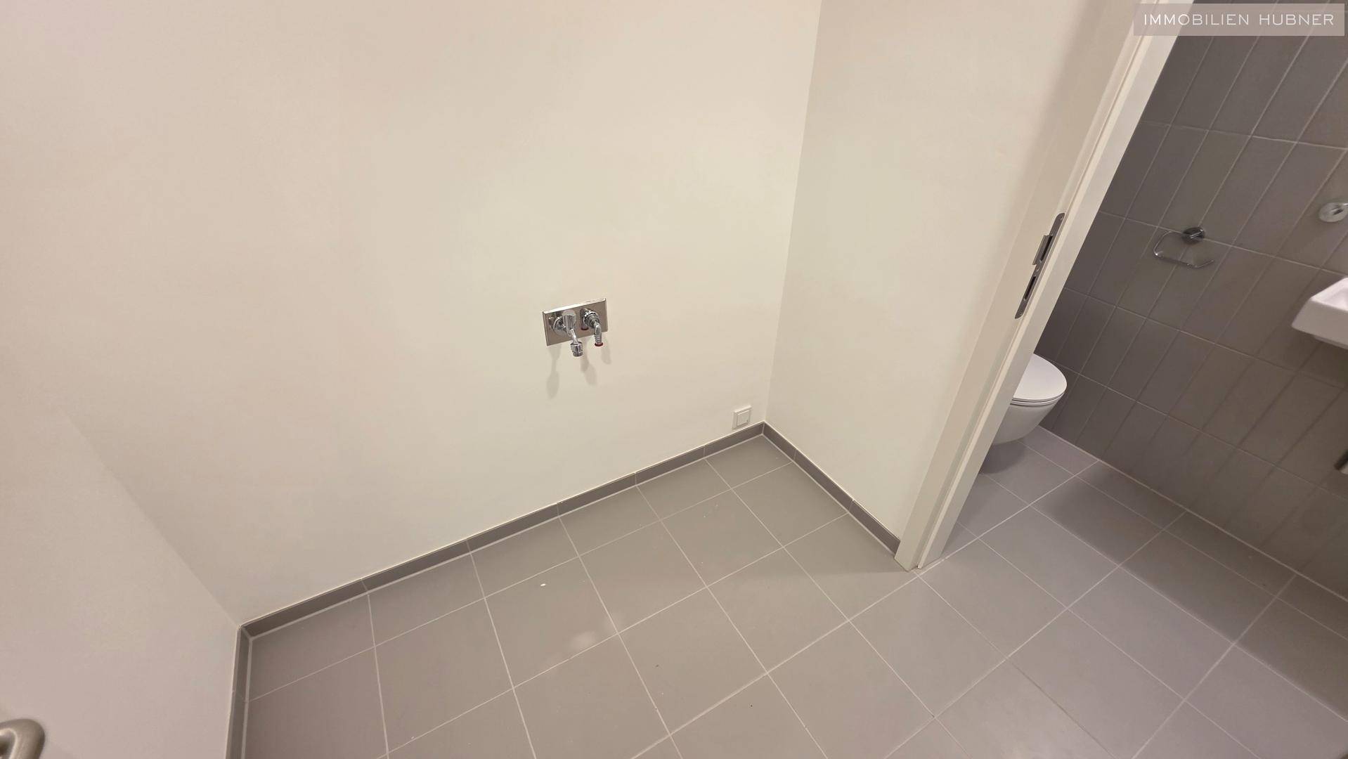 Praktischer Abstellraum mit Fliesenboden und Anschlüssen für Waschmaschine oder Trockner.