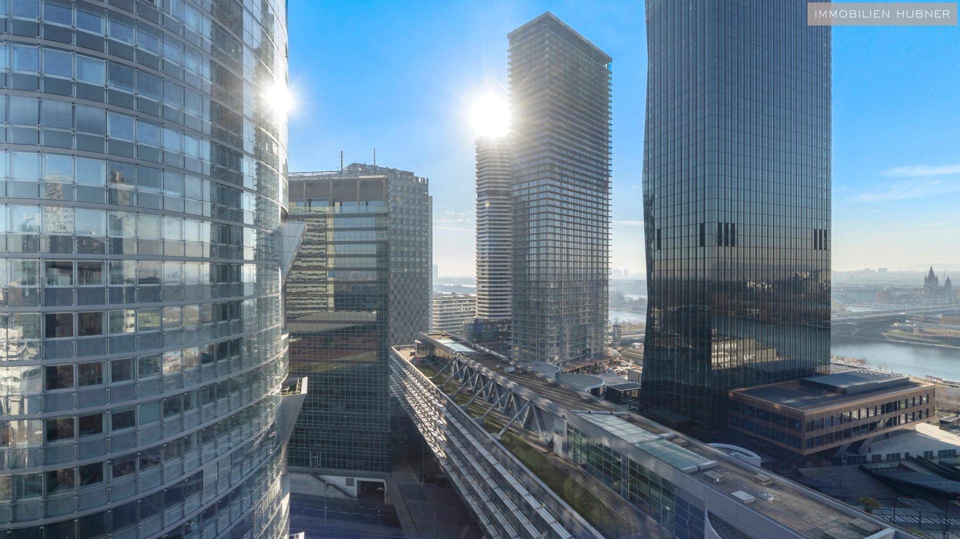 Panoramablick auf die Skyline von Wien mit glänzenden Hochhäusern und der Donau bei Sonnenschein.
