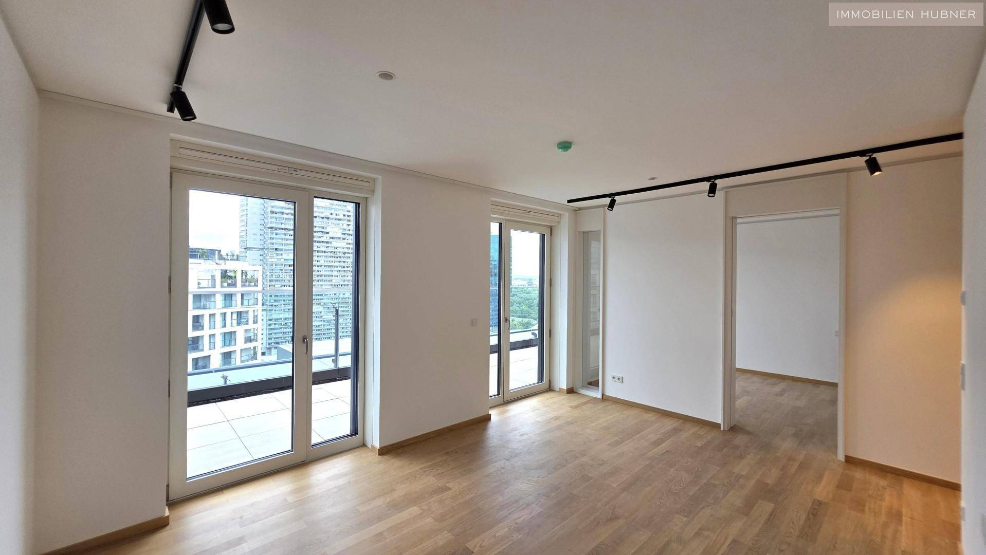 Heller Wohnbereich mit Holzboden und mehreren Fenstern, die Zugang zu einem Balkon bieten und viel Licht spenden.
