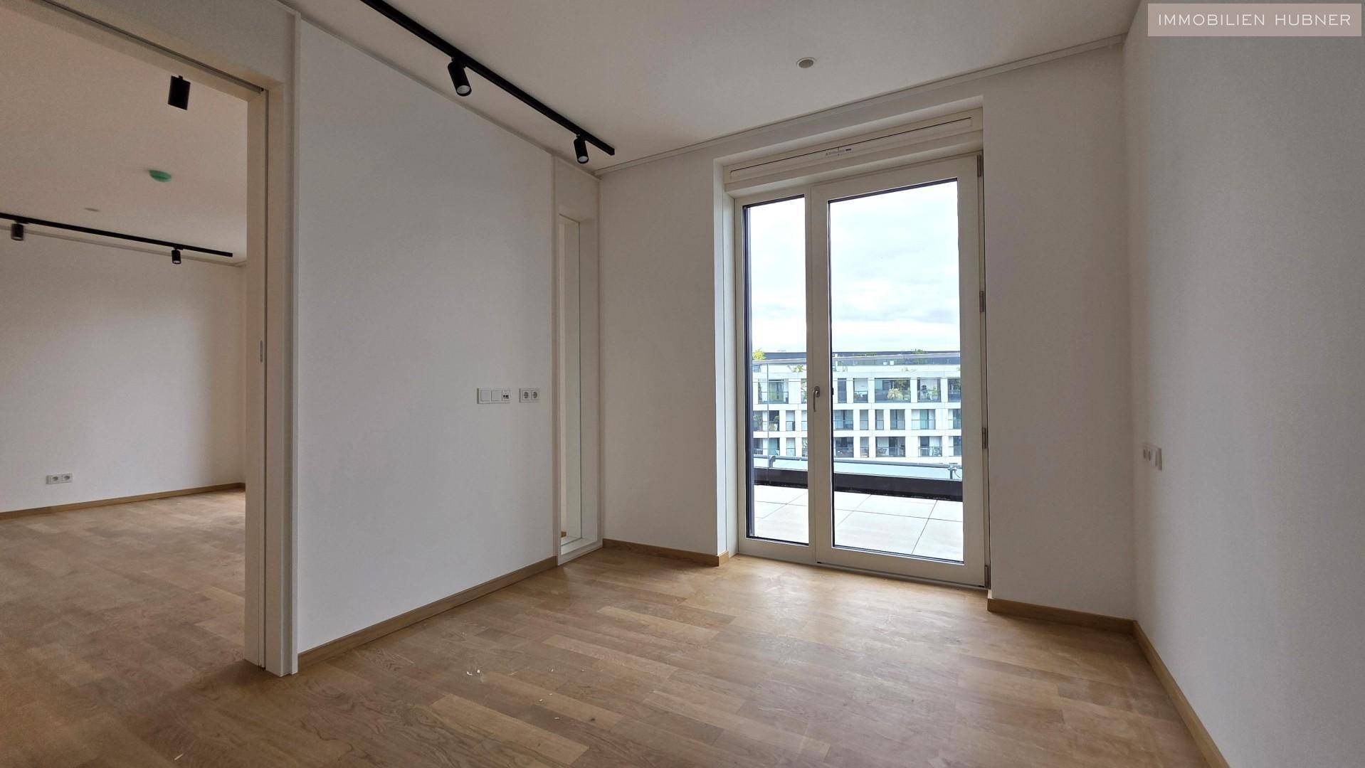 Helles, leeres Zimmer mit Holzboden und Zugang zu einem Balkon, ideal als Schlaf- oder Arbeitszimmer.
