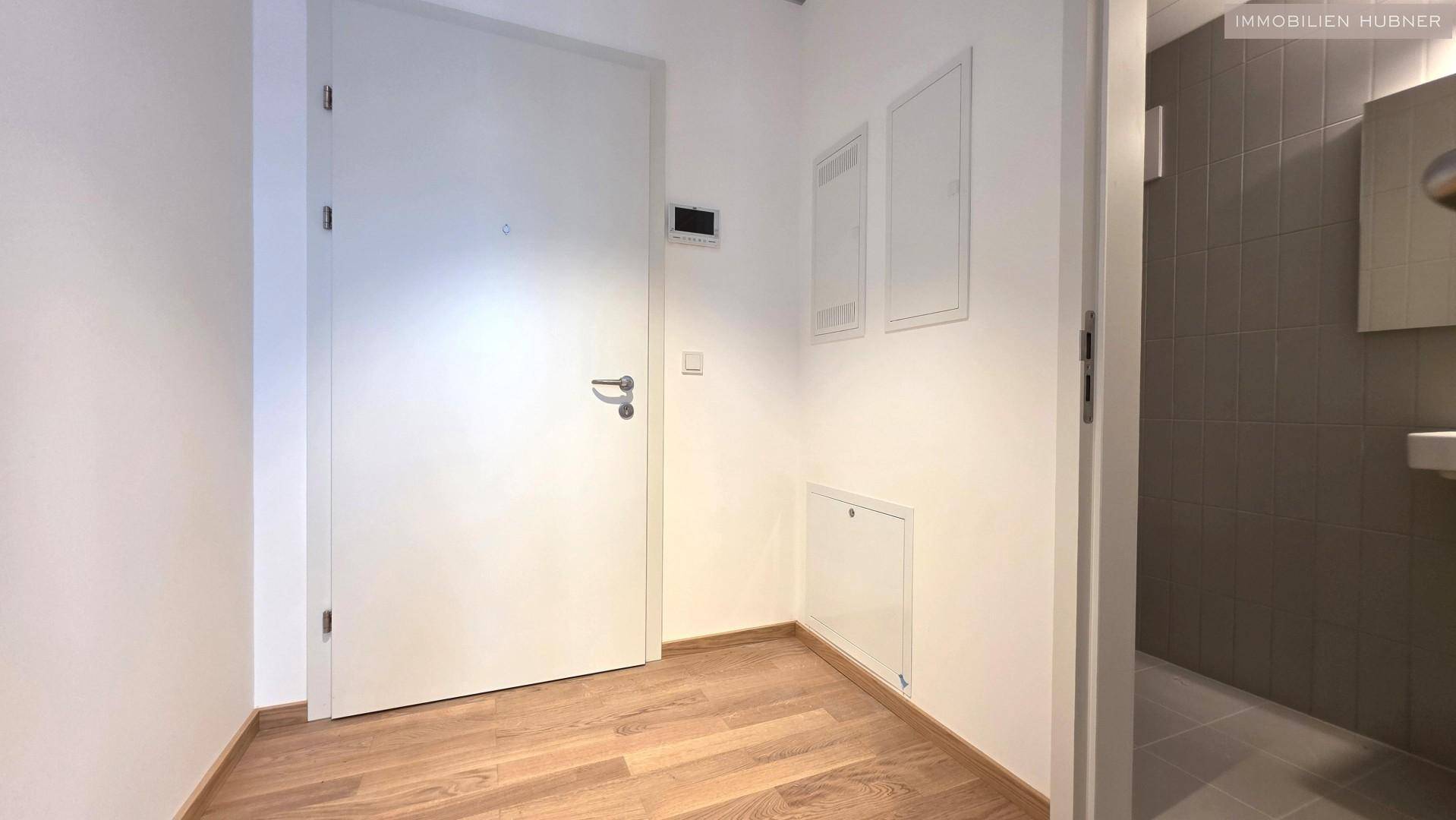 Eingangsbereich mit Holzboden und weißer Tür, führt zu einem gefliesten Badezimmer oder WC.