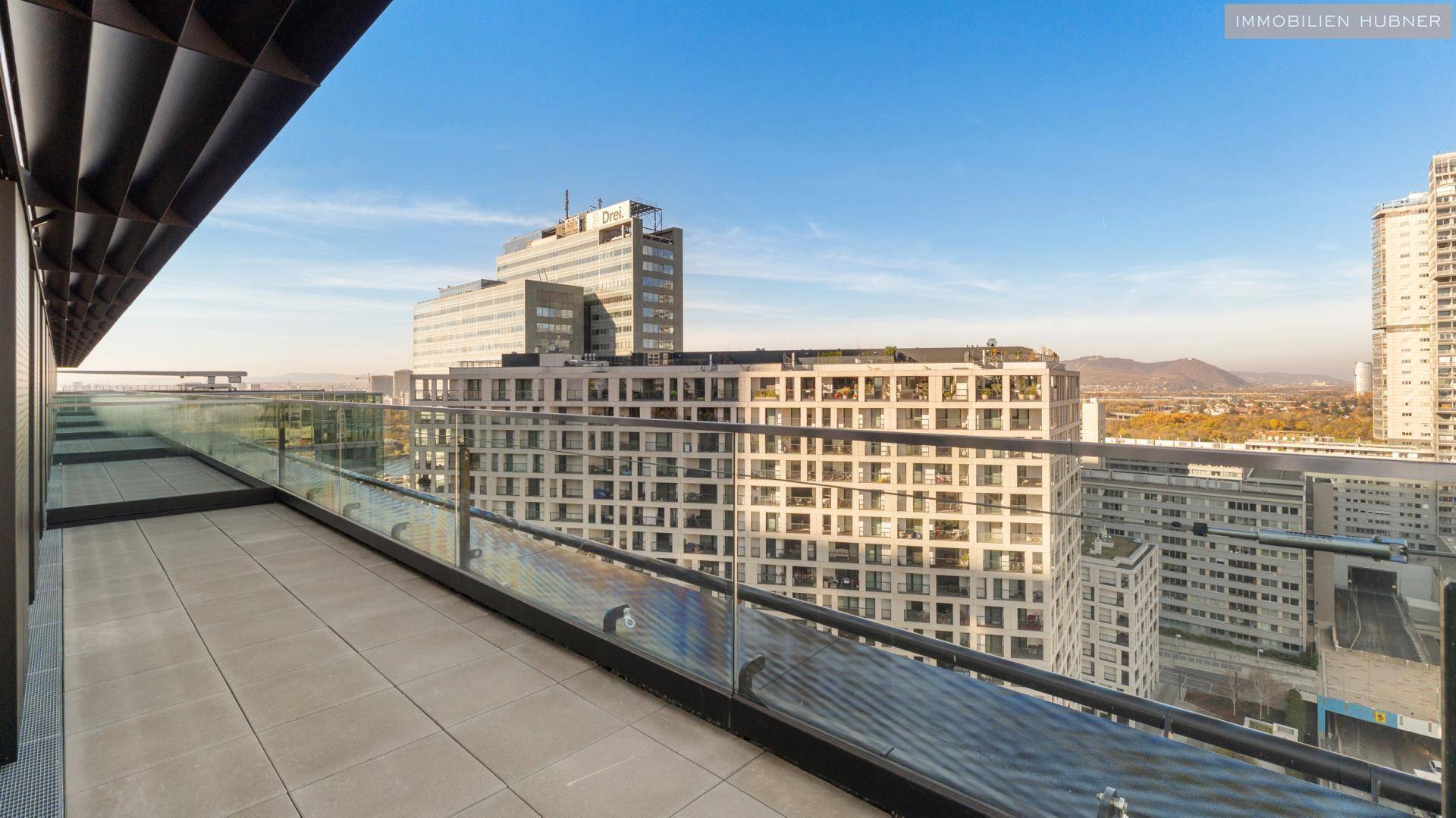 Weitläufige Dachterrasse mit Fliesenboden und Glasgeländer, bietet einen beeindruckenden Blick auf die Stadt.