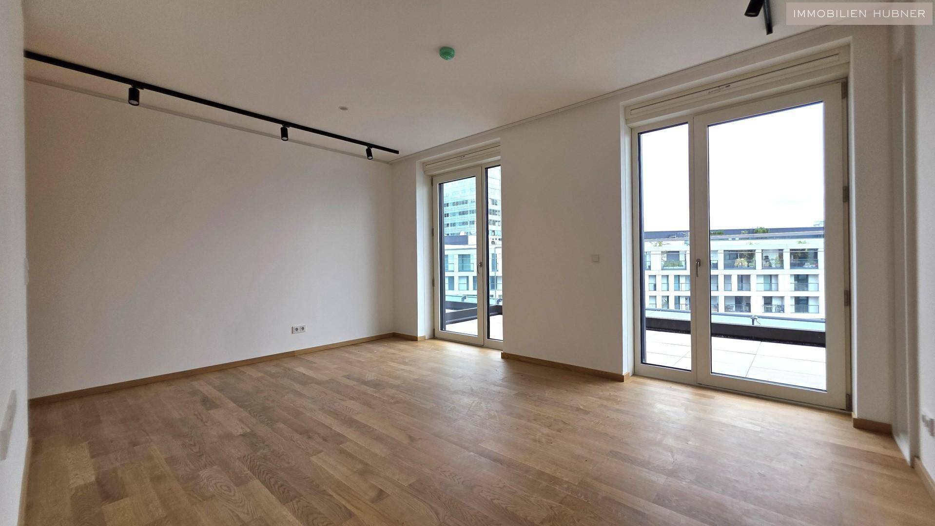 Geräumiger, heller Raum mit Holzboden und zwei Zugängen zu einem Außenbereich, ideal für Wohnzwecke.