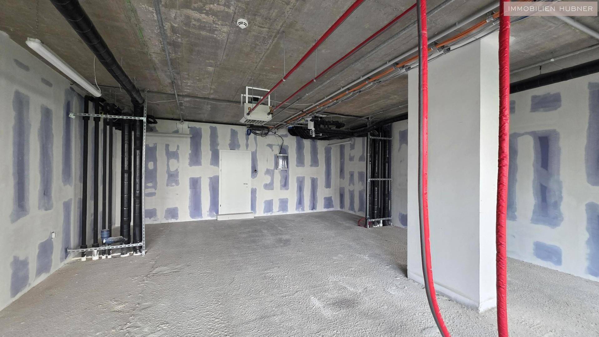 Rohbau eines Gewerberaums mit sichtbaren Installationen und vorbereiteten Wänden für den Innenausbau.