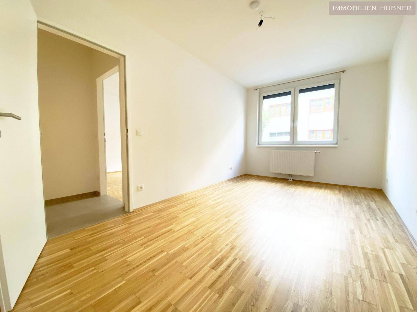 Helles Schlafzimmer mit Parkettboden und Fenster, bereit zur individuellen Gestaltung.