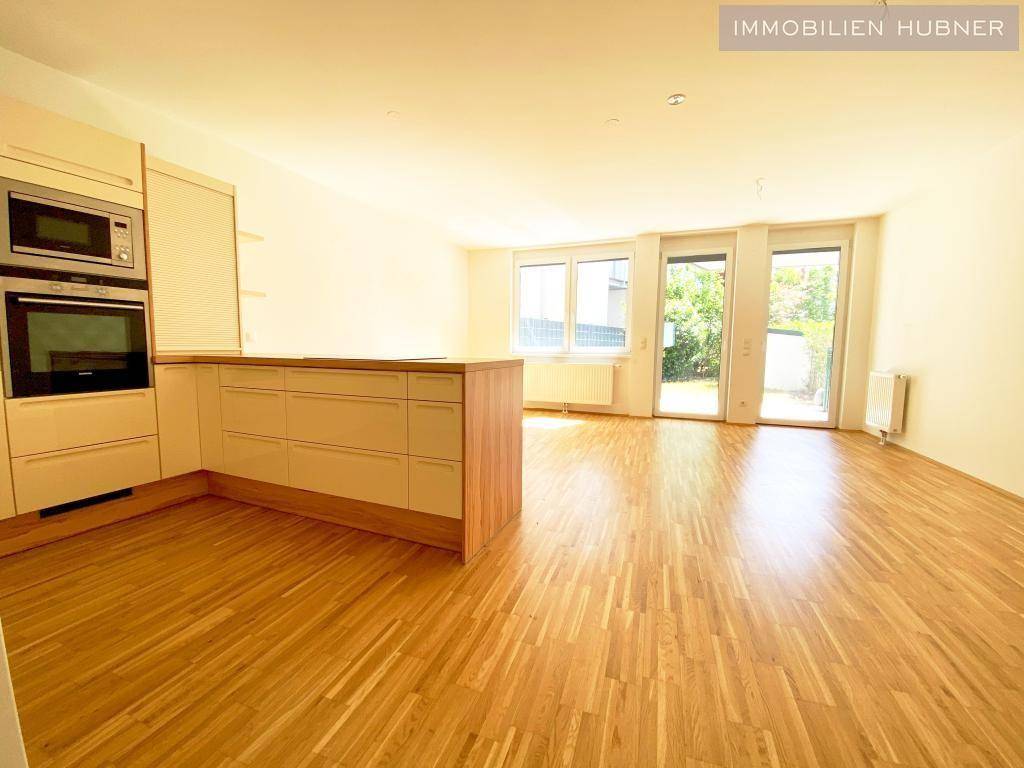 Offener Wohnbereich mit integrierter Küche, Parkettboden und großen Fenstern zum Garten.