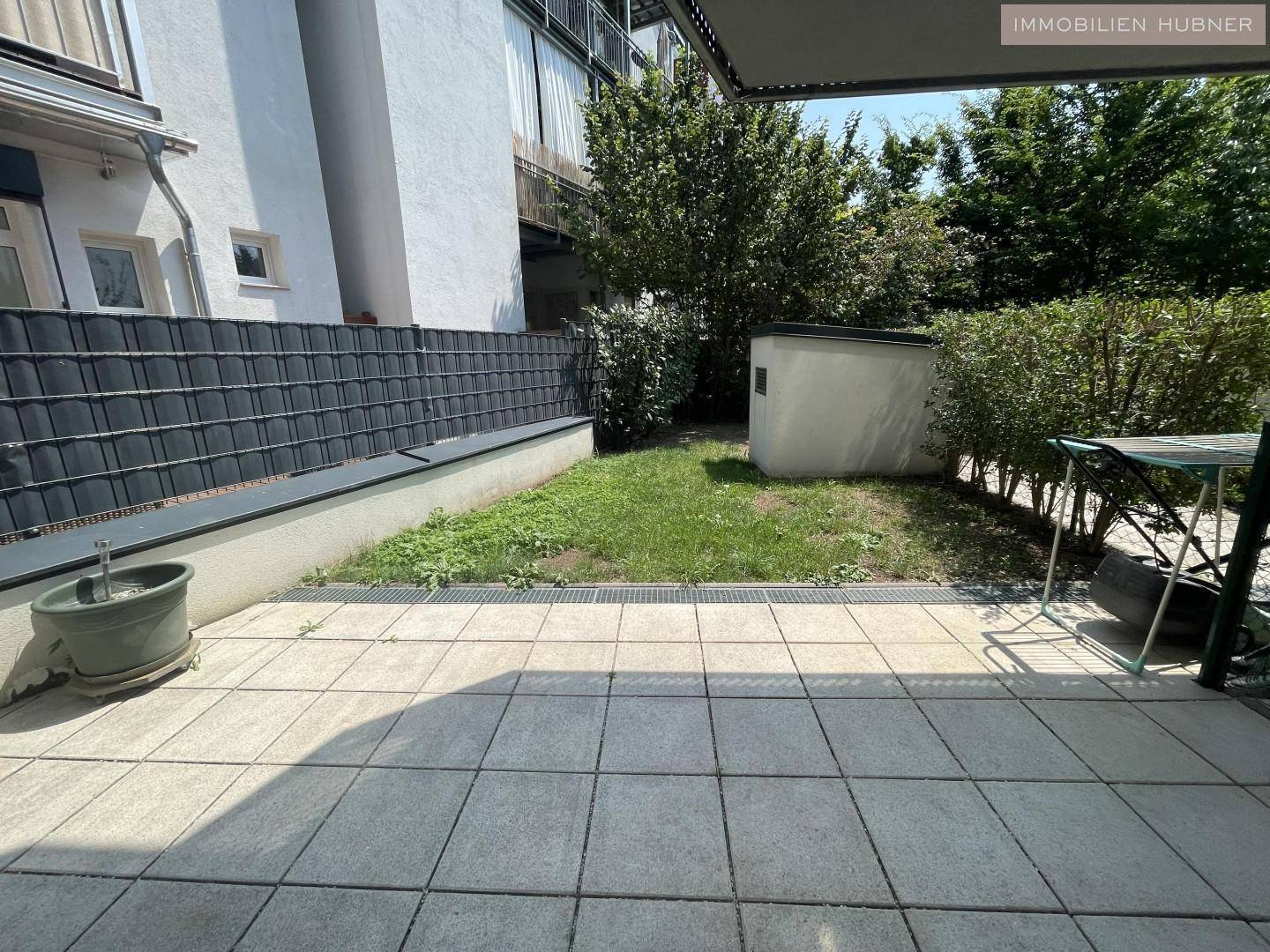Ruhige Terrasse mit Gartenbereich, umgeben von Hecken und einem kleinen Gartenhaus.