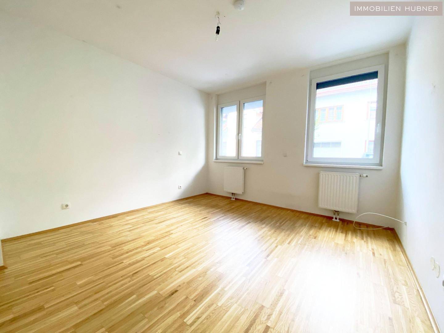 Geräumiges Schlafzimmer mit zwei Fenstern und hellem Parkettboden.
