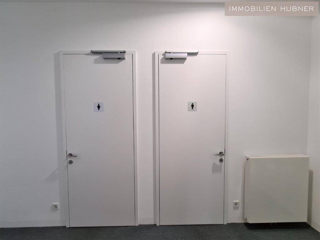 Zwei weiße Türen in einem schlichten Flur, wahrscheinlich zu Toiletten führend, mit einem Heizkörper daneben.