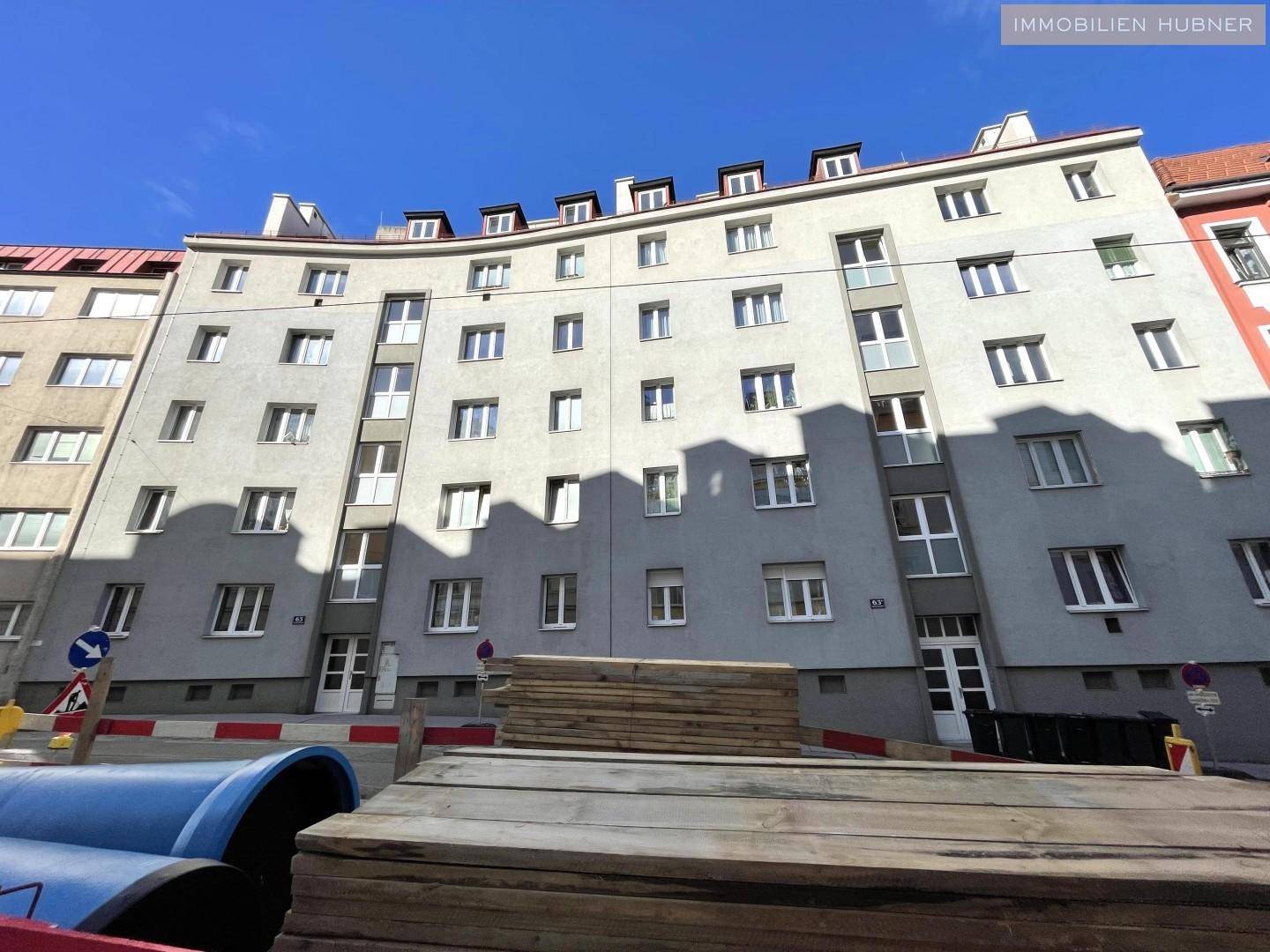 Mehrstöckiges Wohngebäude mit zahlreichen Fenstern und Balkonen unter blauem Himmel.