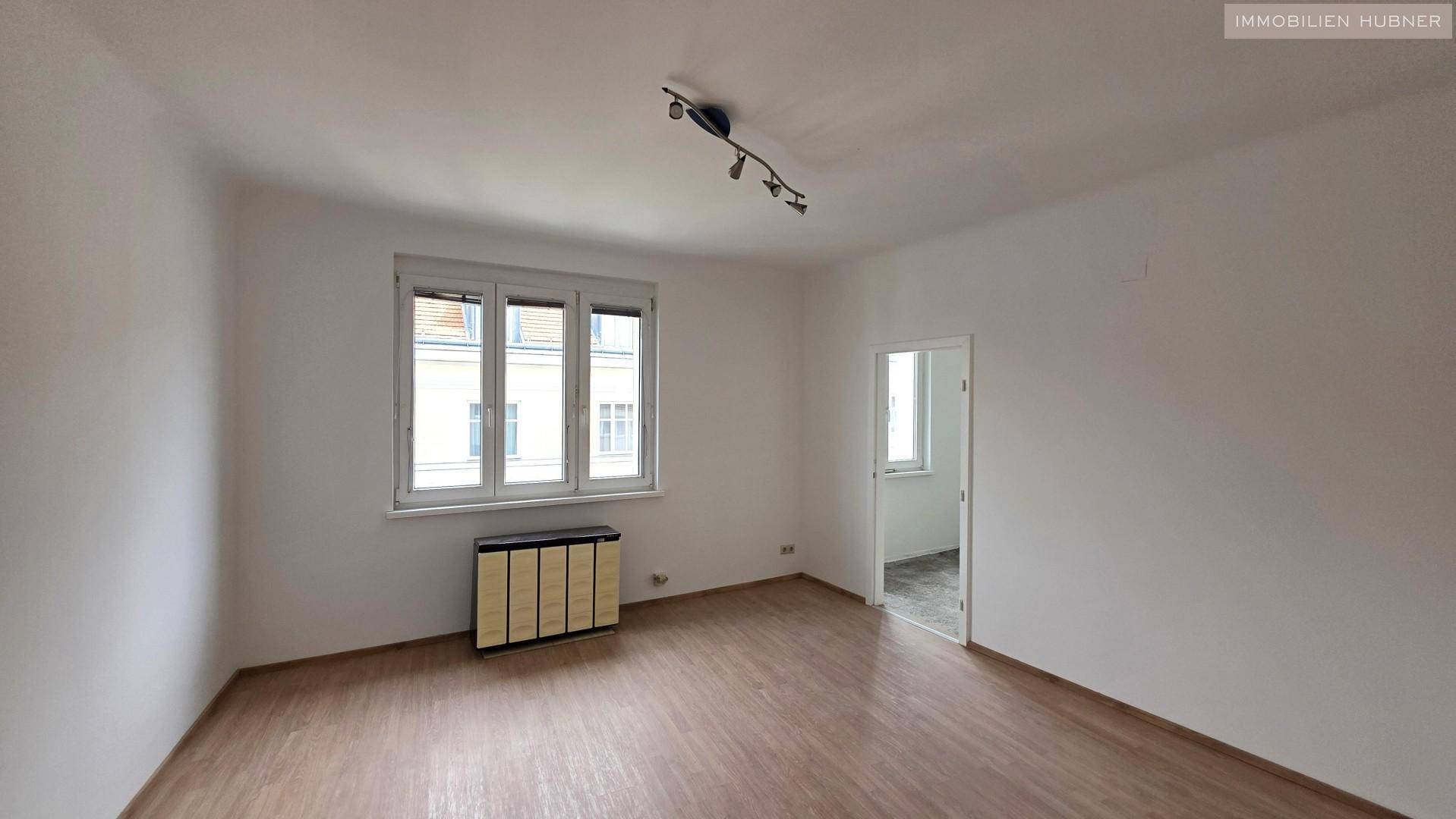 Geräumiges Zimmer mit Laminatboden, Fenster und Heizkörperverkleidung, ideal für Wohnzwecke.