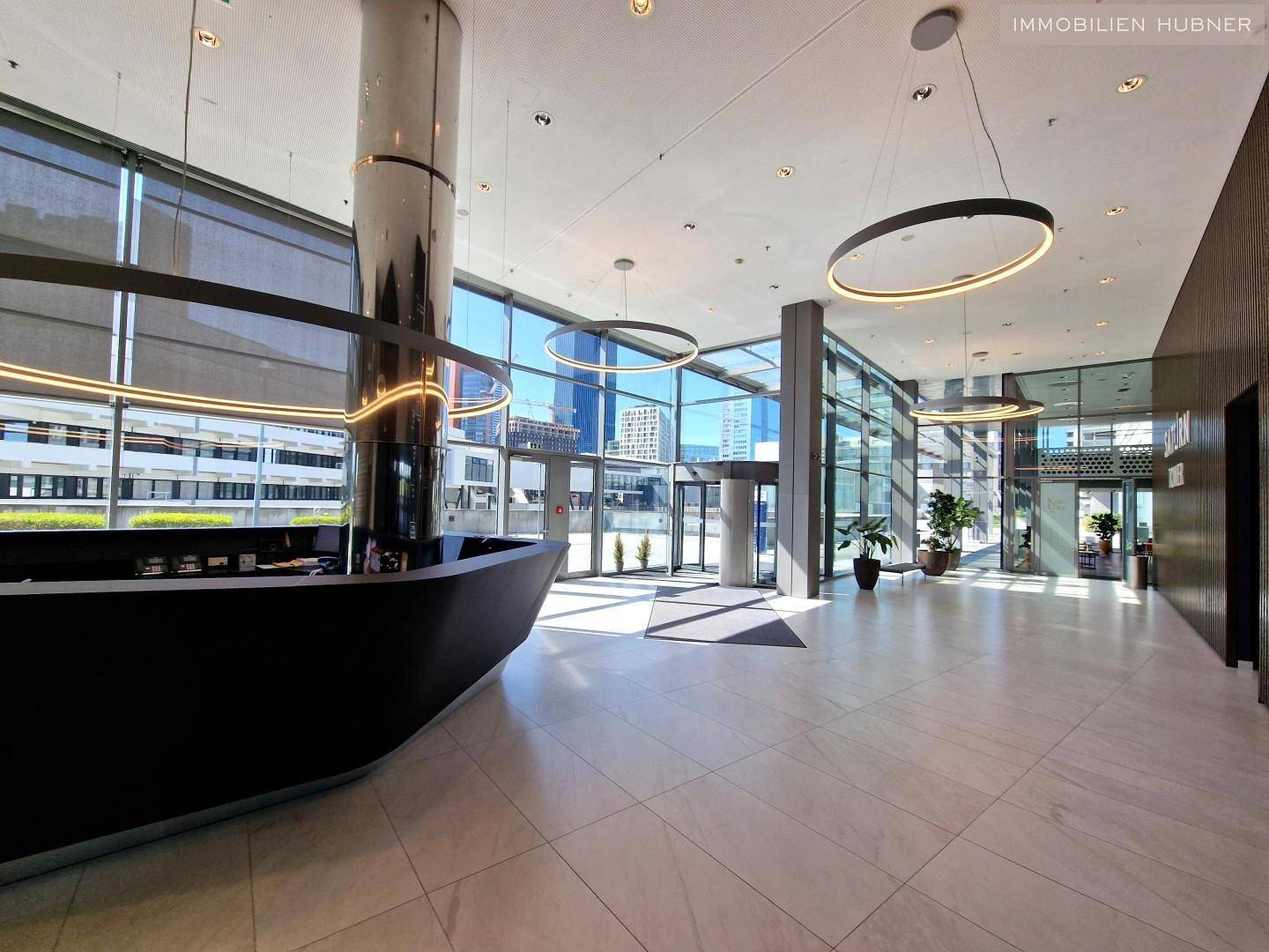 Elegante Lobby mit modernem Empfangstresen, hohen Decken und großen Glasfronten für viel Licht.