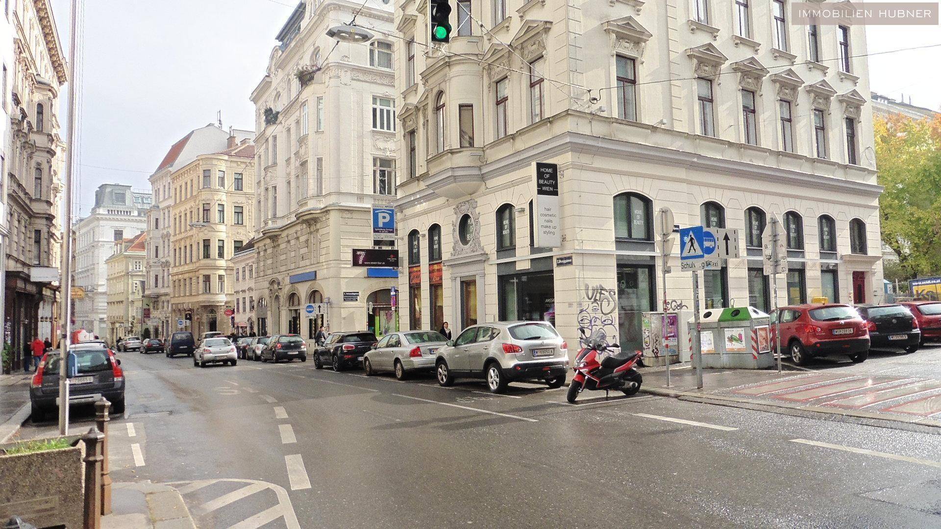 Straßenansicht des historischen Gebäudes mit parkenden Autos und städtischem Treiben.