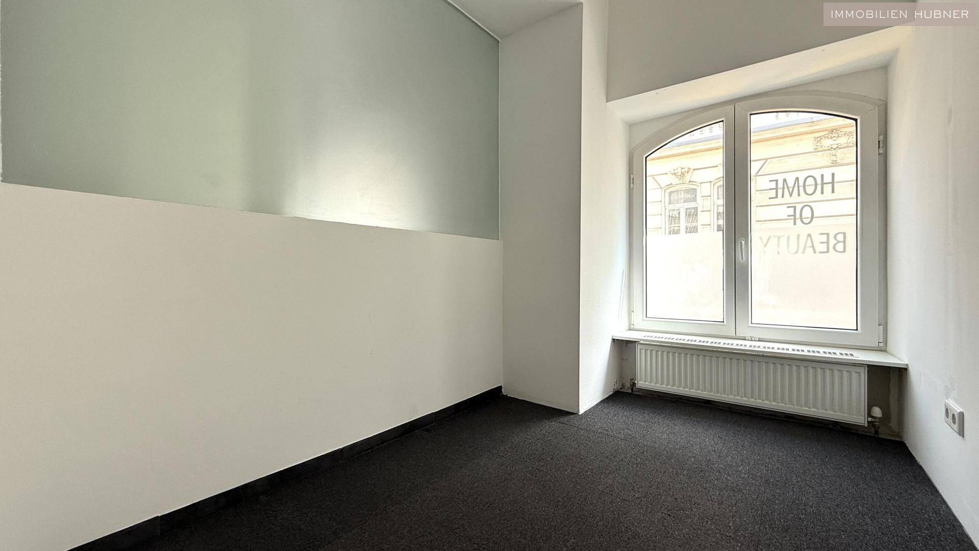 Raum mit einem großen Bogenfenster, Teppichboden und zweifarbigen Wänden in Weiß und Hellgrau.