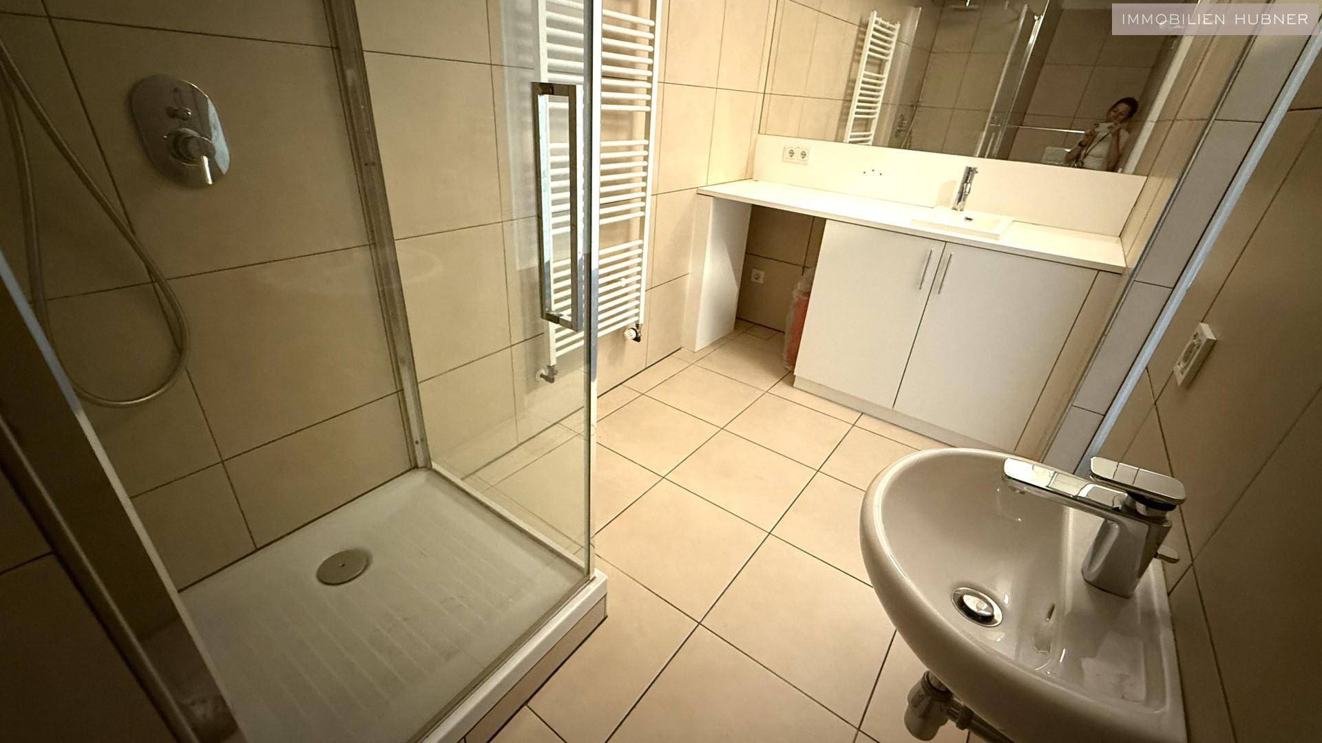 Badezimmer mit beigefarbenen Fliesen, einer Duschkabine, Waschbecken und einem praktischen Waschtischunterschrank.