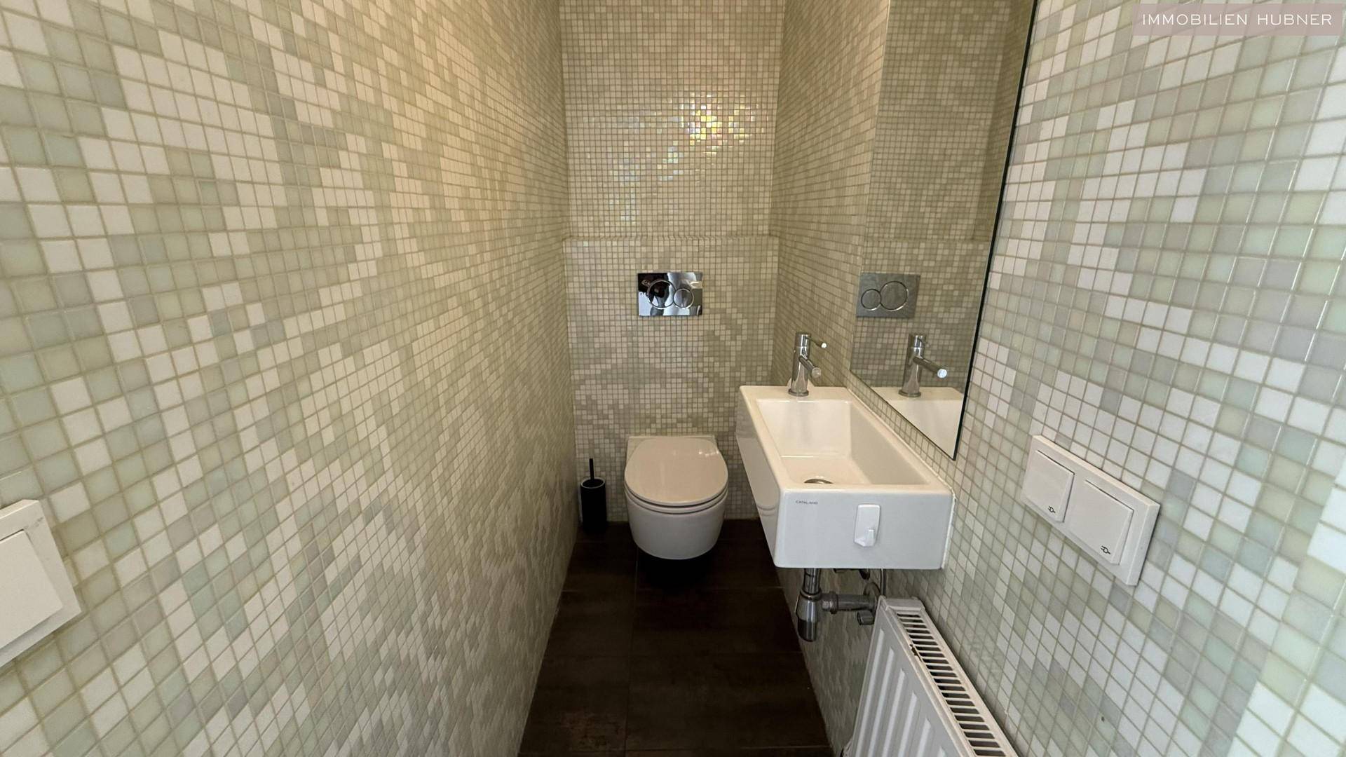 Modernes Gäste-WC mit Mosaikfliesen, einem eleganten Waschbecken und einer wandhängenden Toilette.