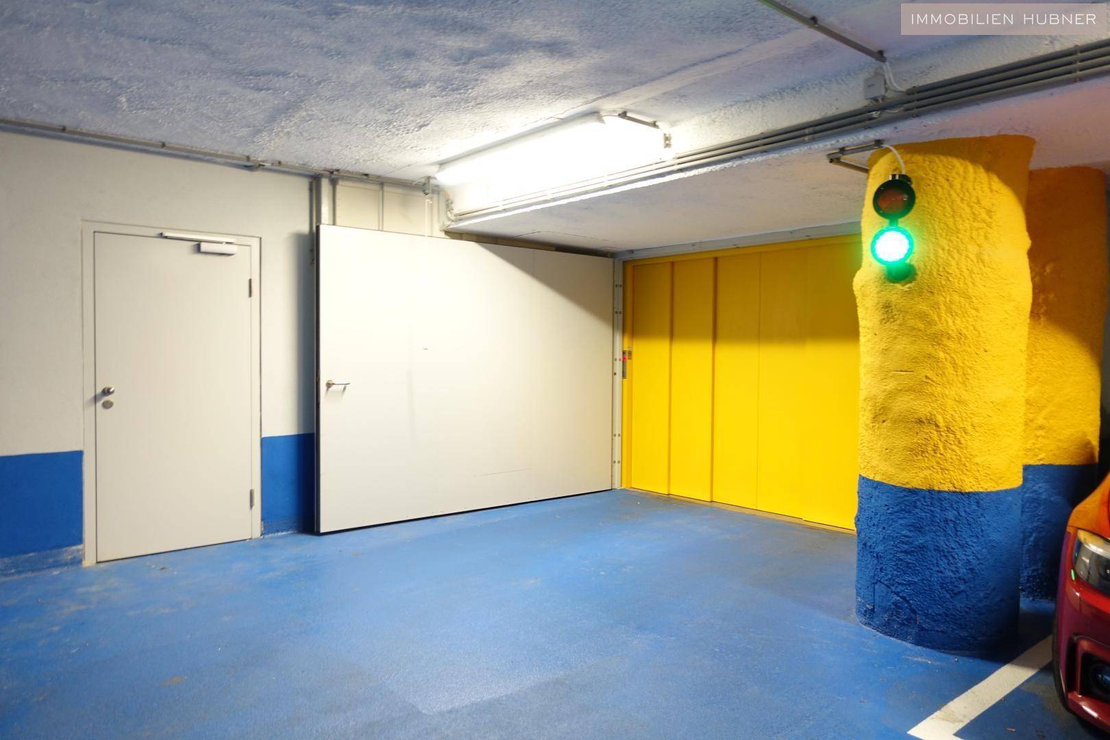 Innenansicht einer Tiefgarage mit blauem Boden, gelben Säulen und einer Ampel zur Verkehrsregelung.