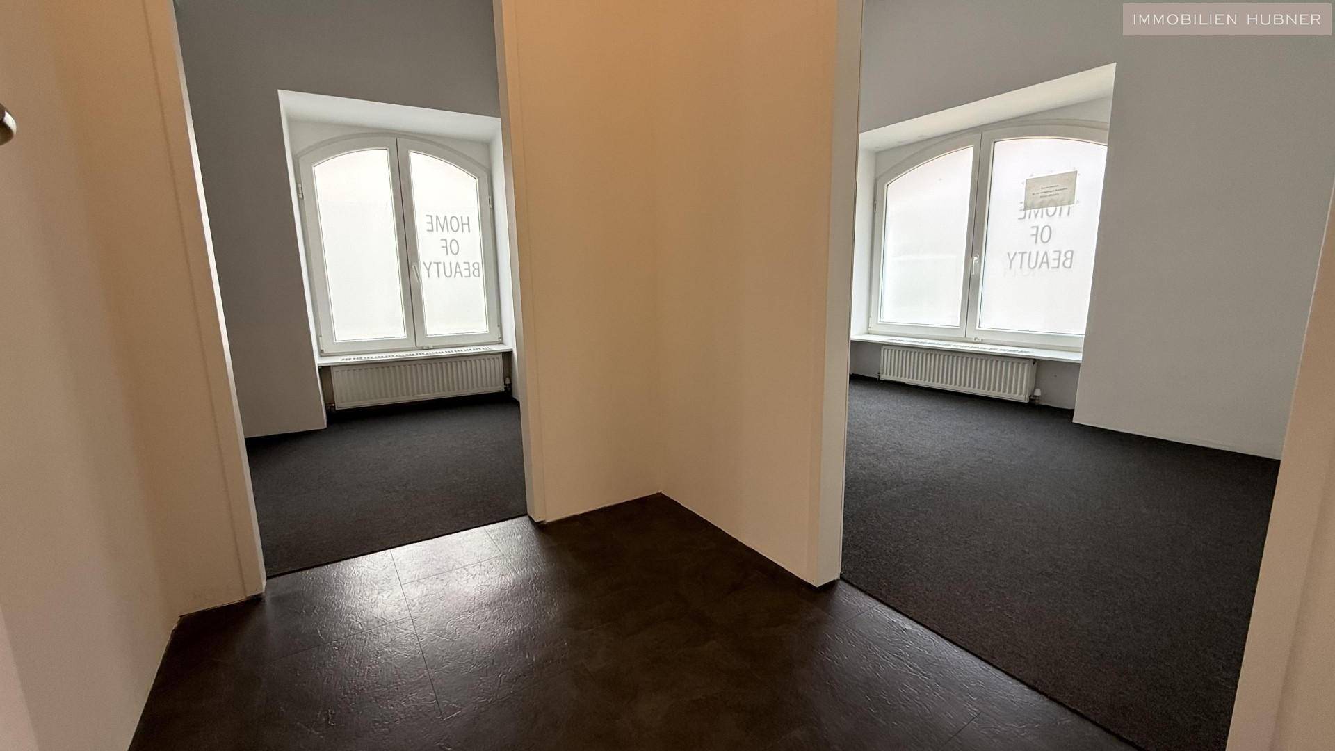 Blick in zwei separate, helle Räume mit Teppichboden und großen Bogenfenstern, getrennt durch eine Wand.