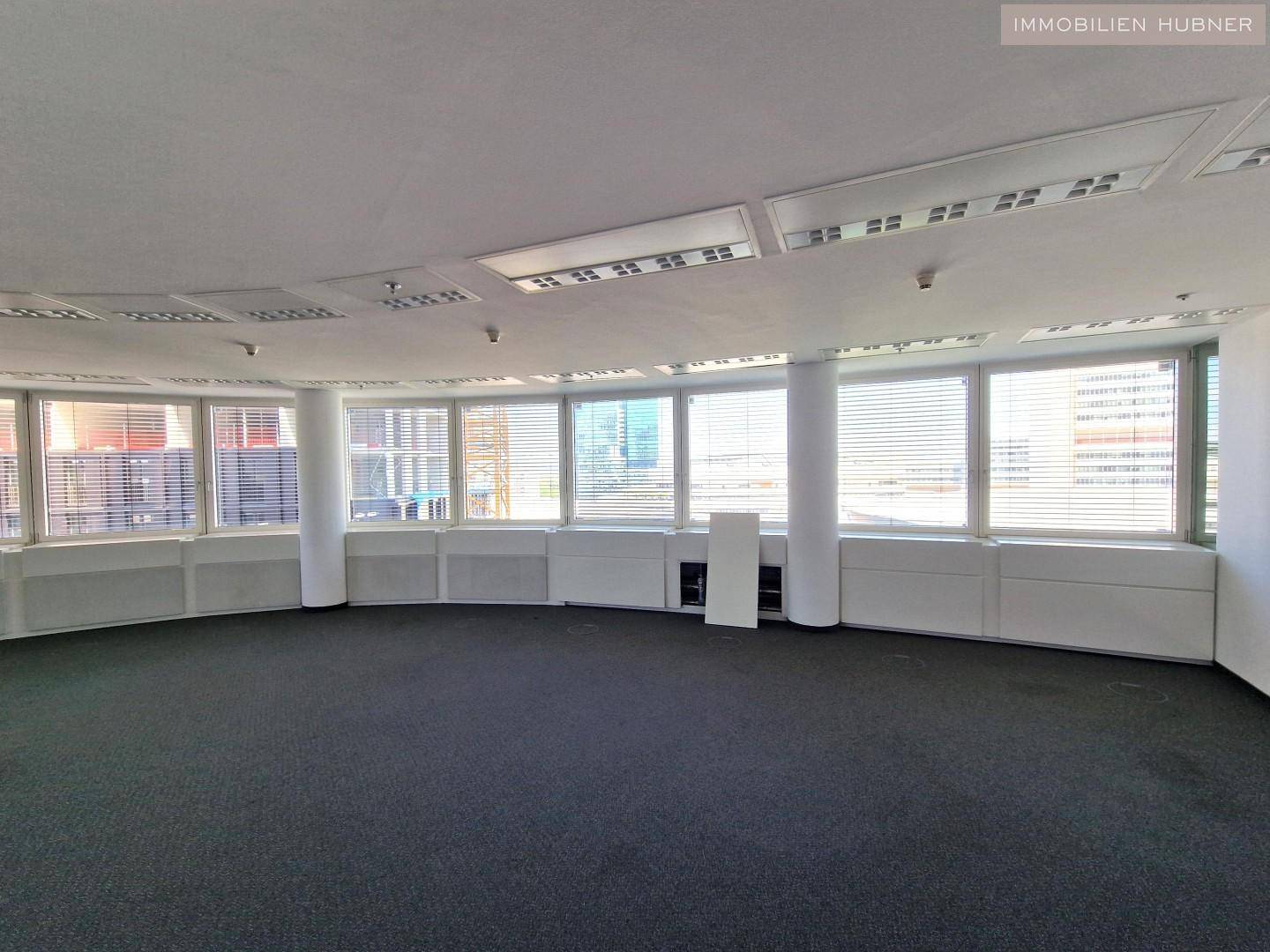 Heller Büroraum mit durchgehenden Fensterfronten und Teppichboden, bereit für individuelle Gestaltung.