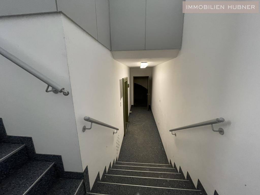 Treppenhaus mit dunklen Stufen und weißen Wänden, ausgestattet mit Handläufen, führt in die unteren Etagen.